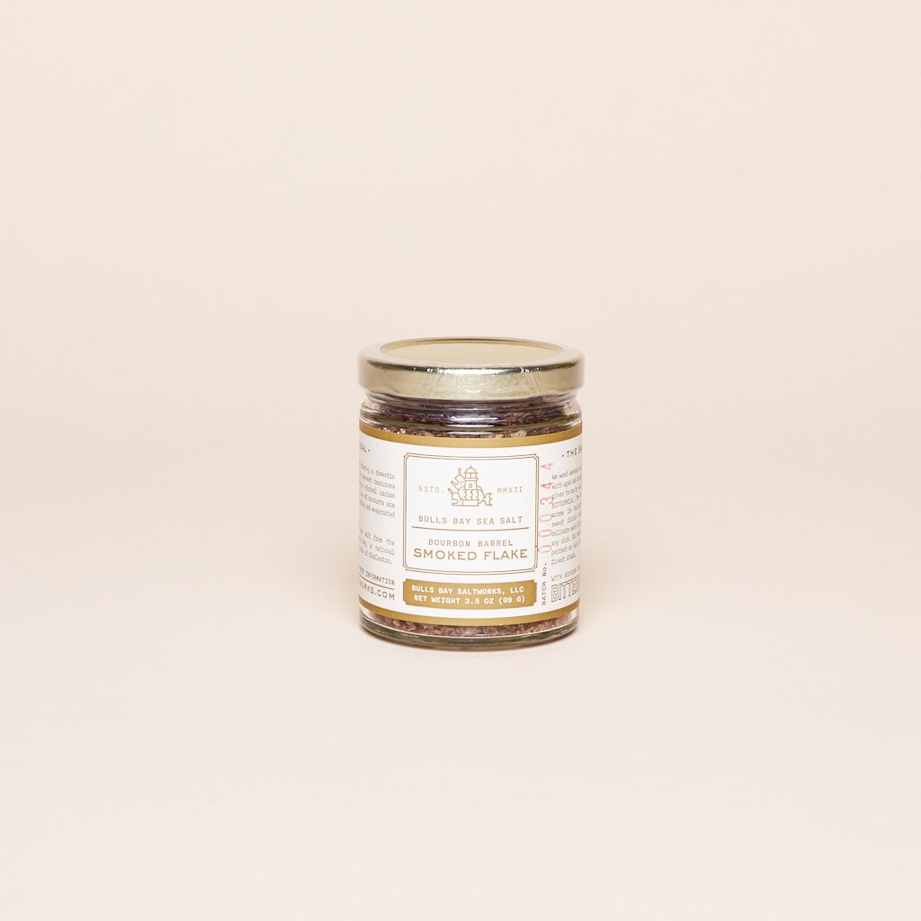 A glass jar with gold lid and white and gold label that identifies the product as smoked flake salt