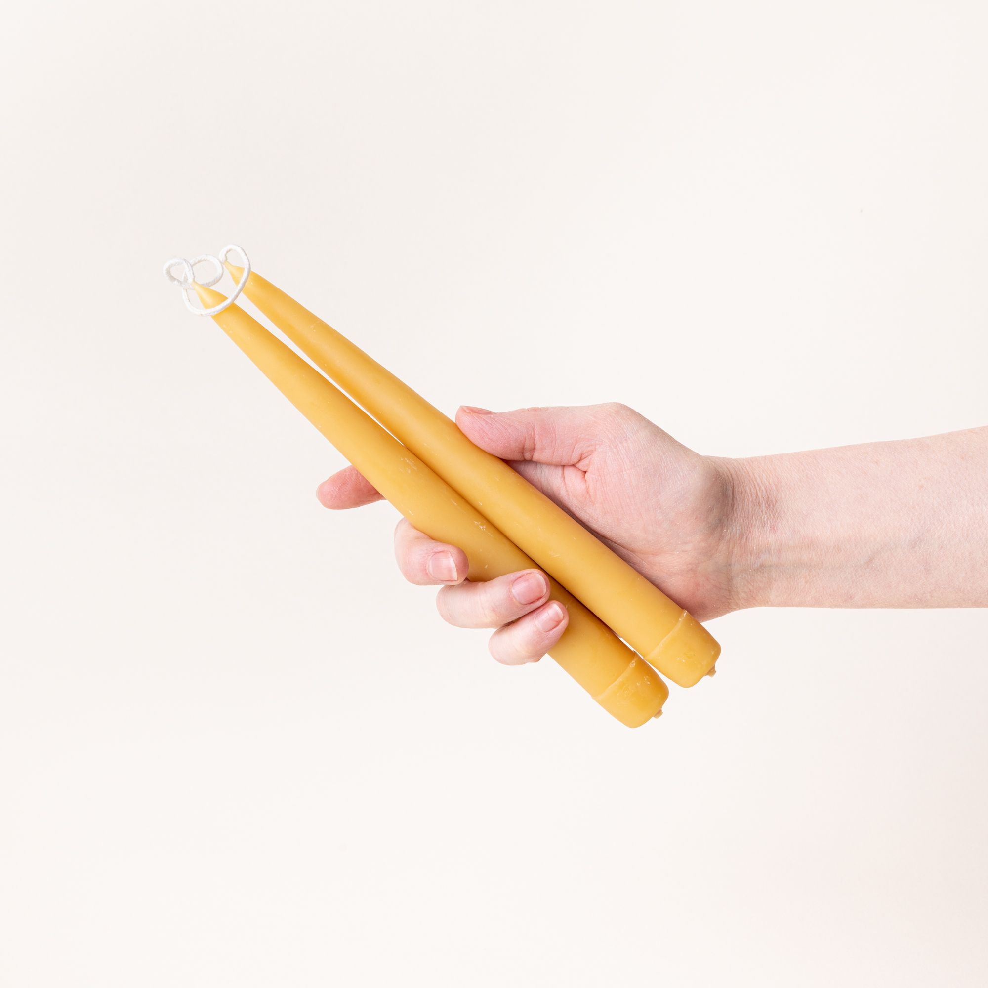 A hand holds a pair of yellow beeswax taper candles