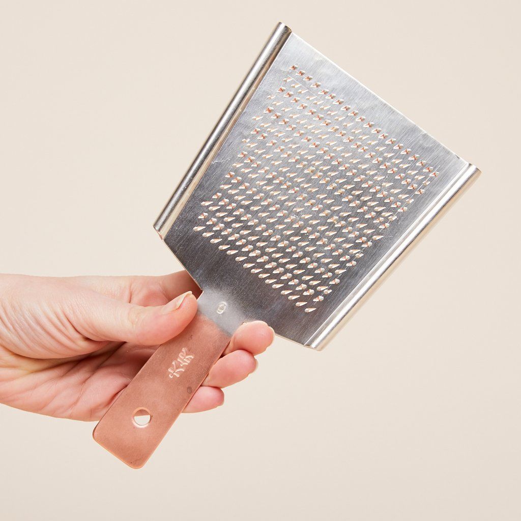 A rectangular metal grater with a copper-colored handle, held in a hand