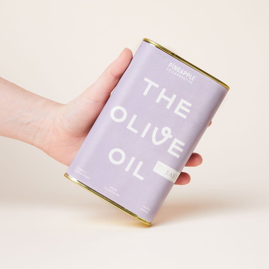 A hand angles the edge of a can of olive oil with a purple label