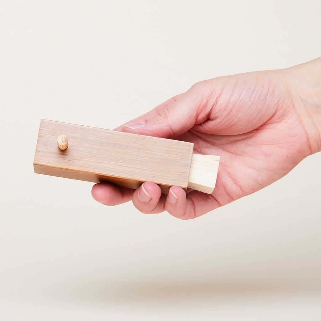 In a hand, there is a rectangular spice dispenser with a peg sticking out of one side and a wood stopper