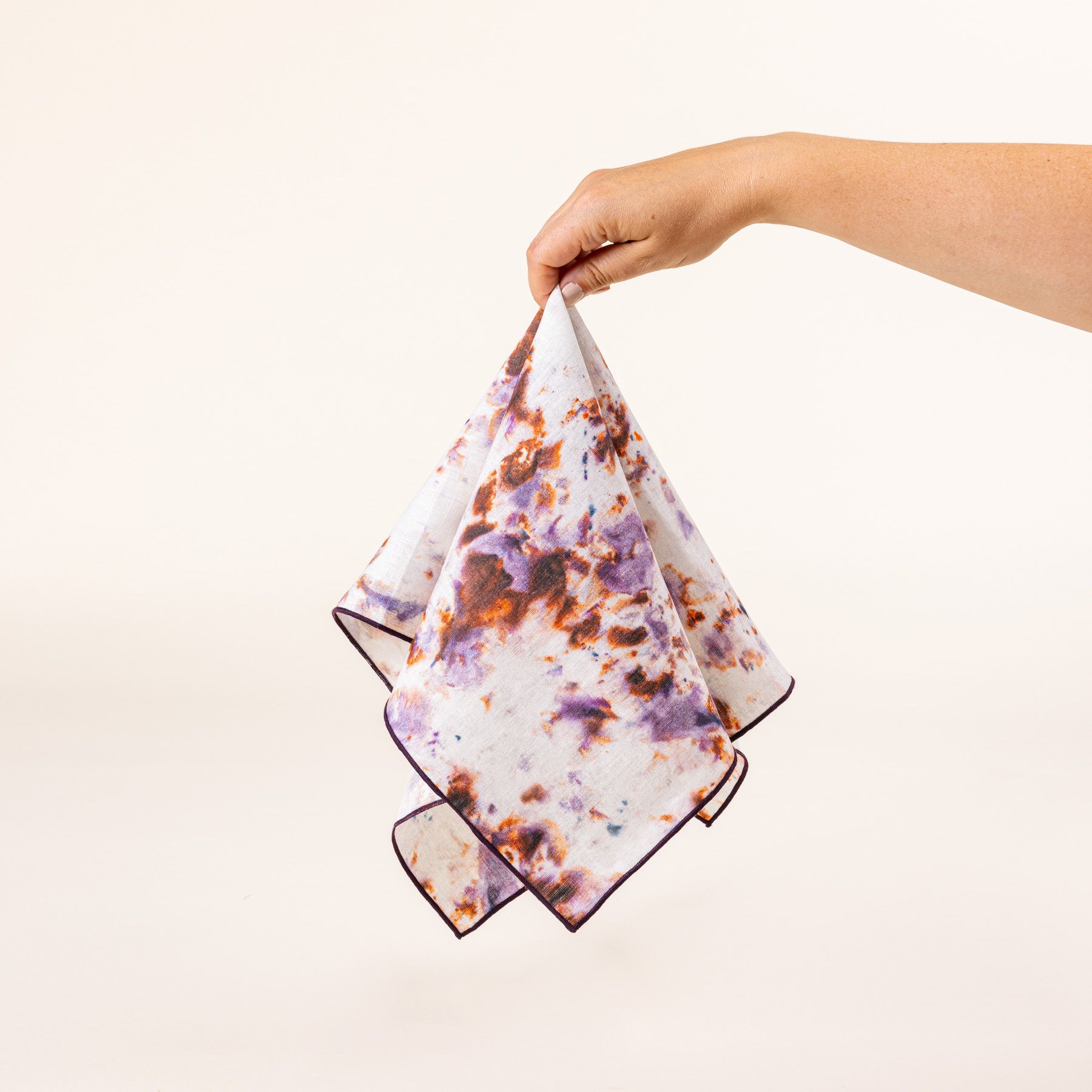 A hand holds a linen napkin in a marbled pattern with white, pink, purple, and orange colors