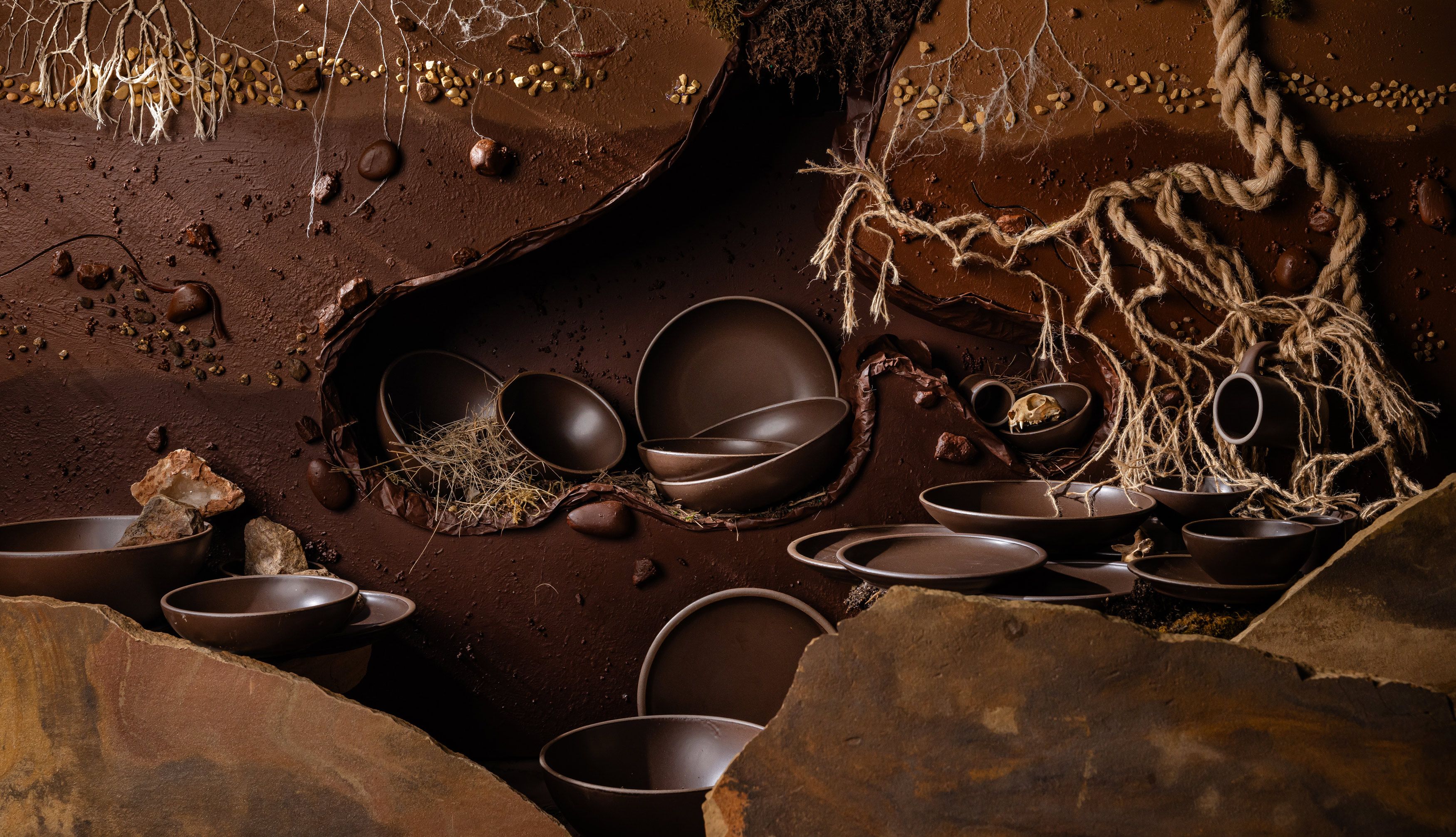 Earthy ground environment with tree roots, rocks, and dirt with various plates and bowls in a dark brown. 