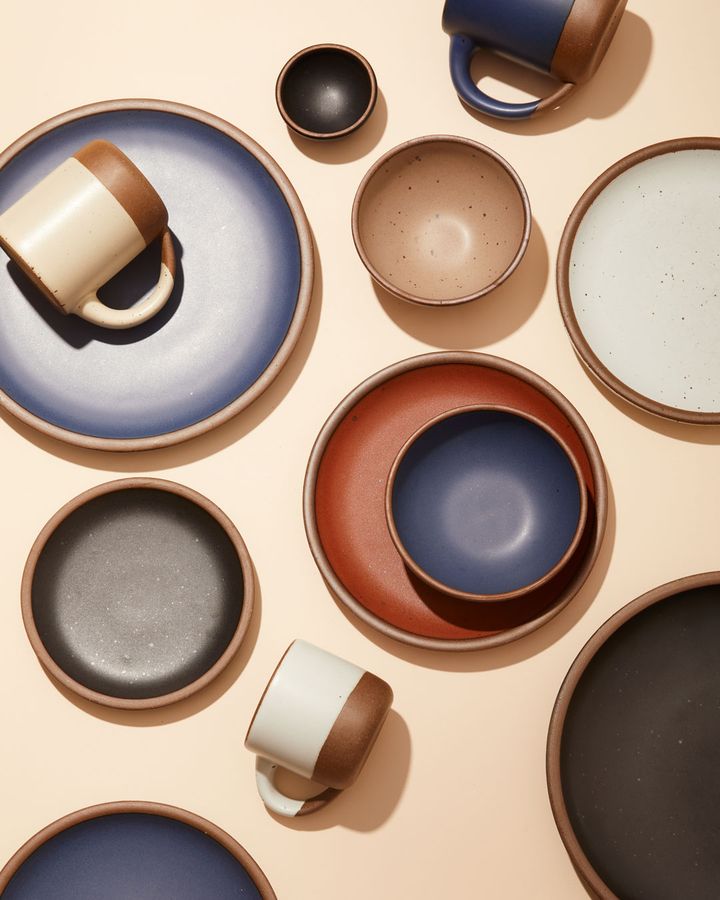 An assortment of ceramic bowls, plates, and mugs in neutral colors, blues, and charcoal.