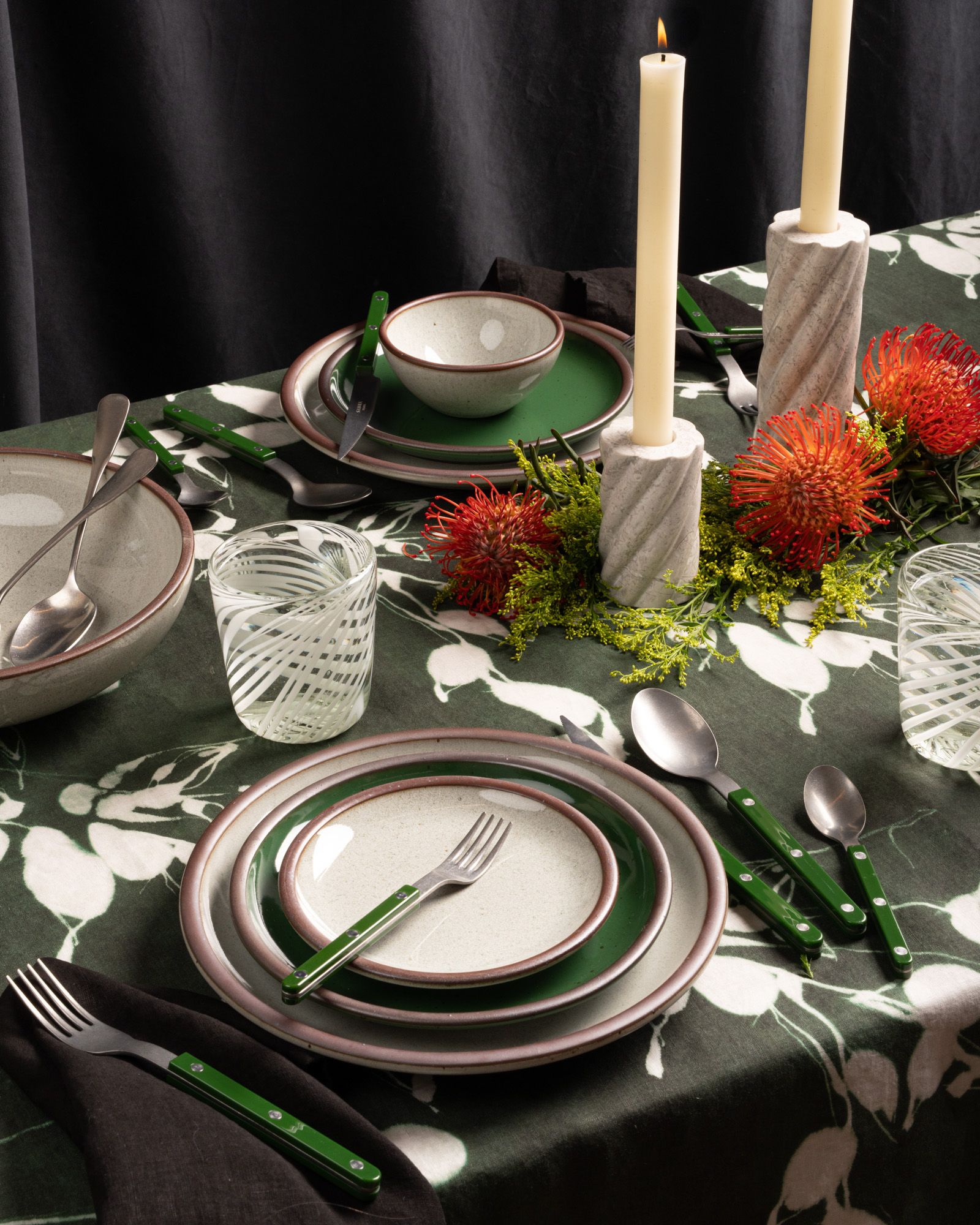 A festive table with ceramic dinnerware in glossy green and icy white colors, swirled glassware, and green flatware.