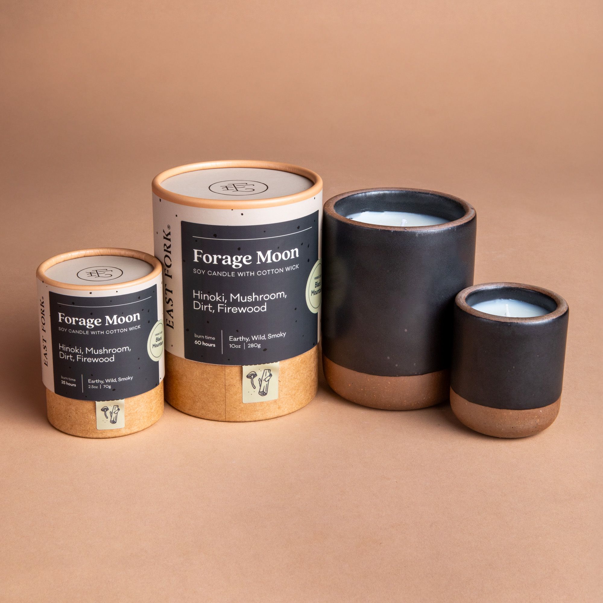Small and large ceramic vessel next to each other in dark charcoal color with candles inside each. Cardboard tube packaging is on the left with branding stickers that say "Forage Moon".