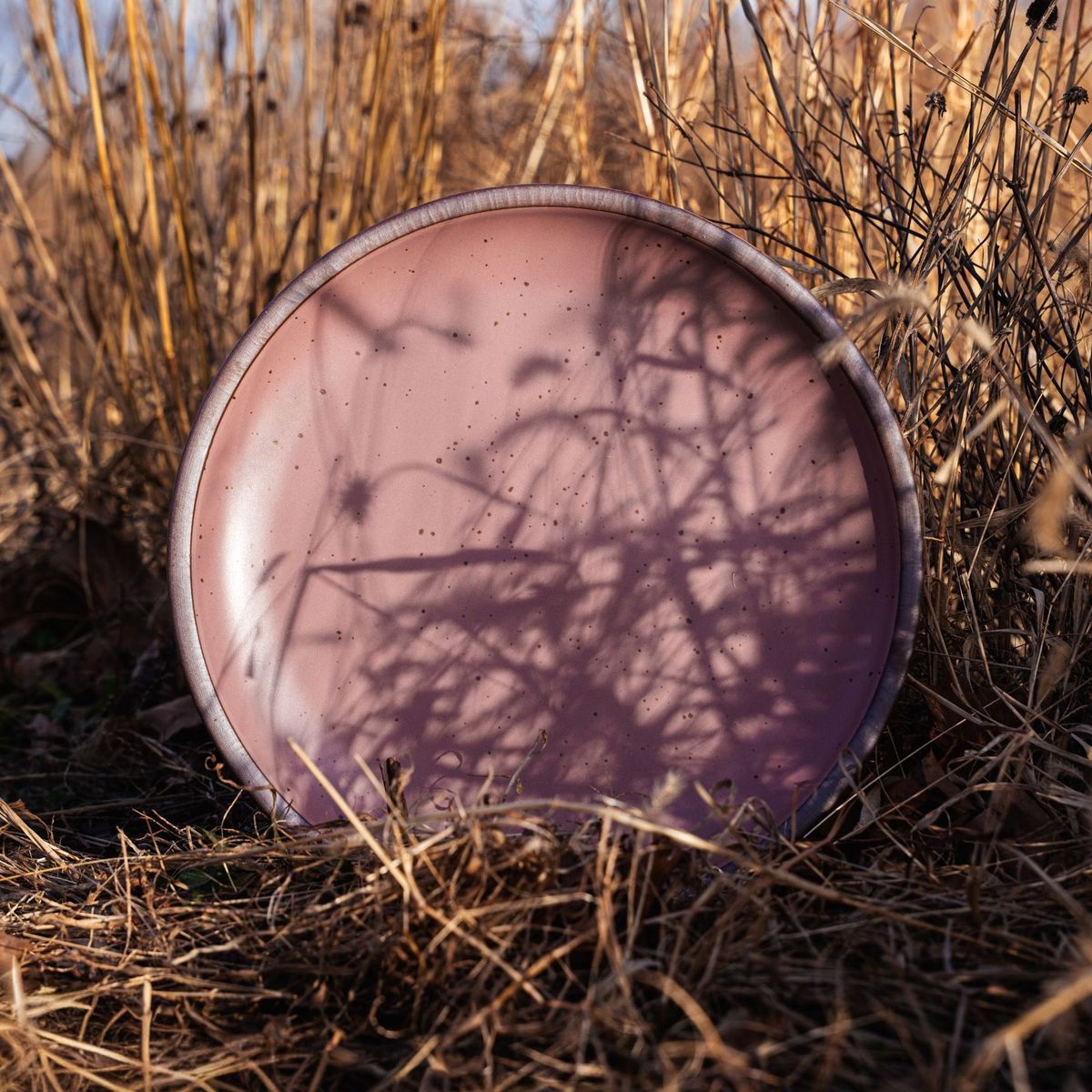 Dusty mauve pink ceramic platter arranged in dry grass and wild plants outdoors.