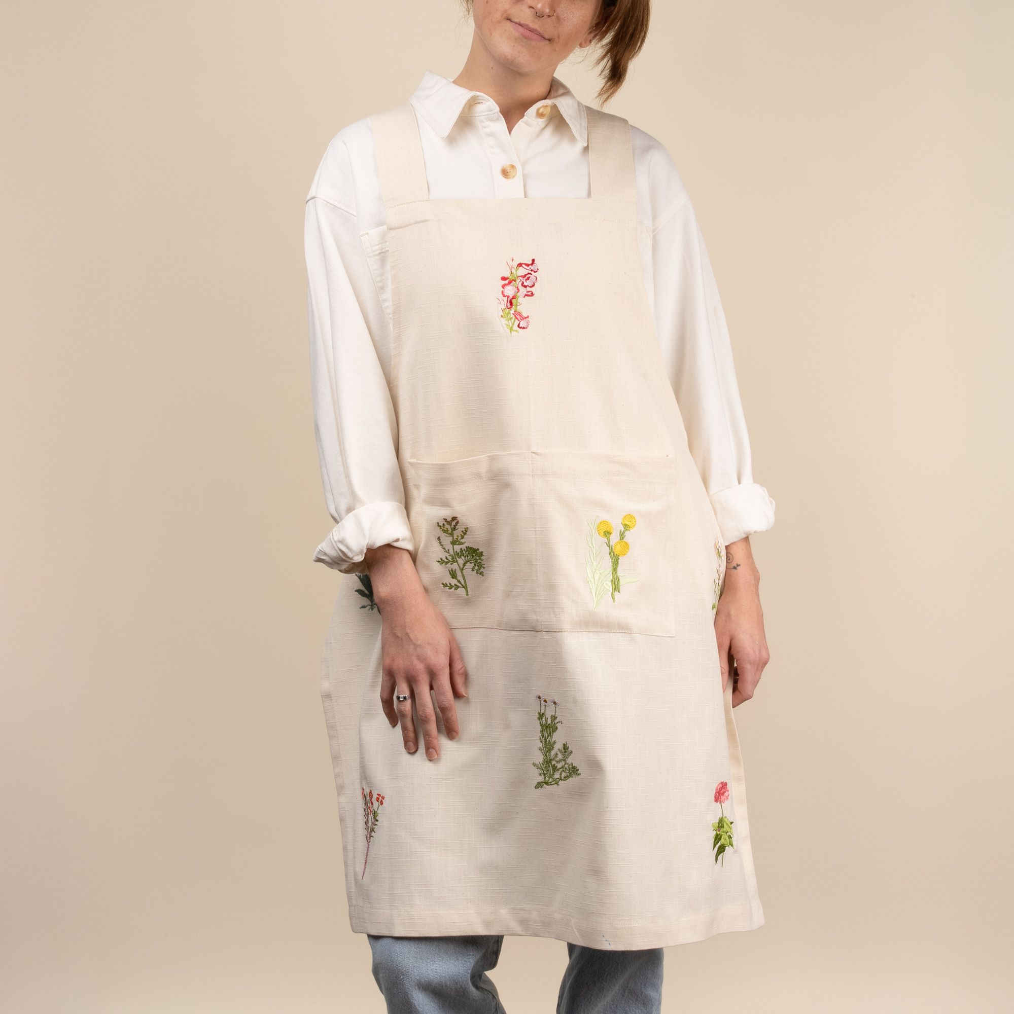 A woman wearing a canvas apron with embroidered flowers on it with large pockets in the front waist.