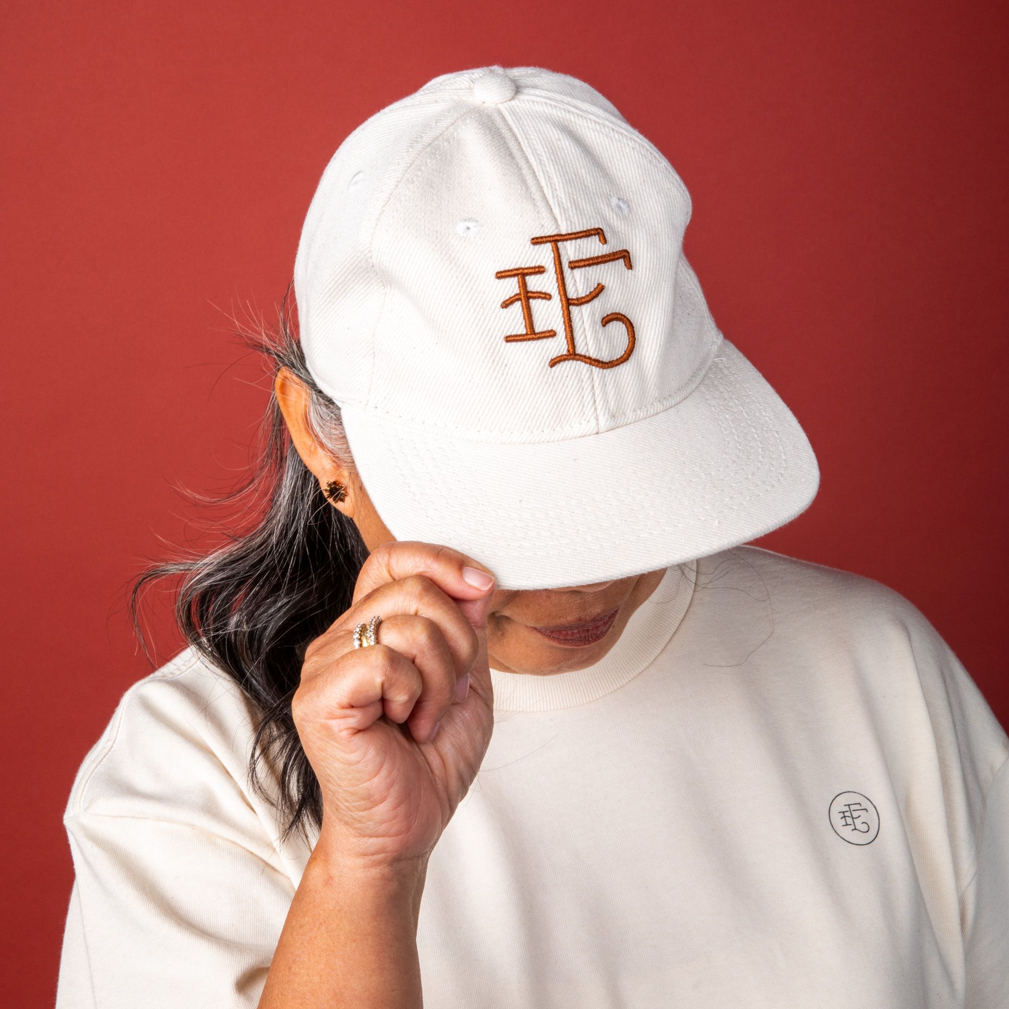 A person wears the white denim baseball hat and shows off the front. The hat has a burnt terracotta stitching of East Fork's logo in a simple cursive - 'EF'.