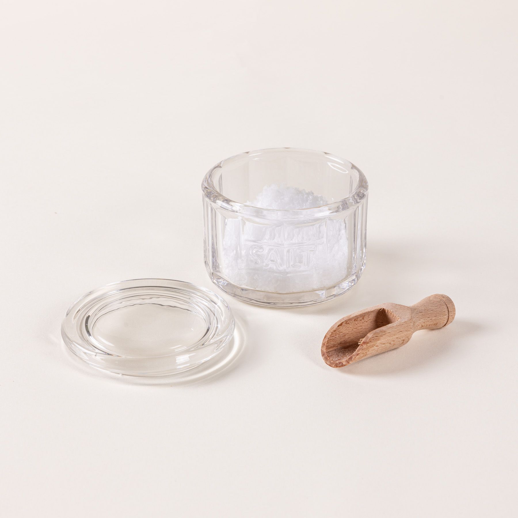 Round glass clear salt canister filled with salt and a small wooden scoop