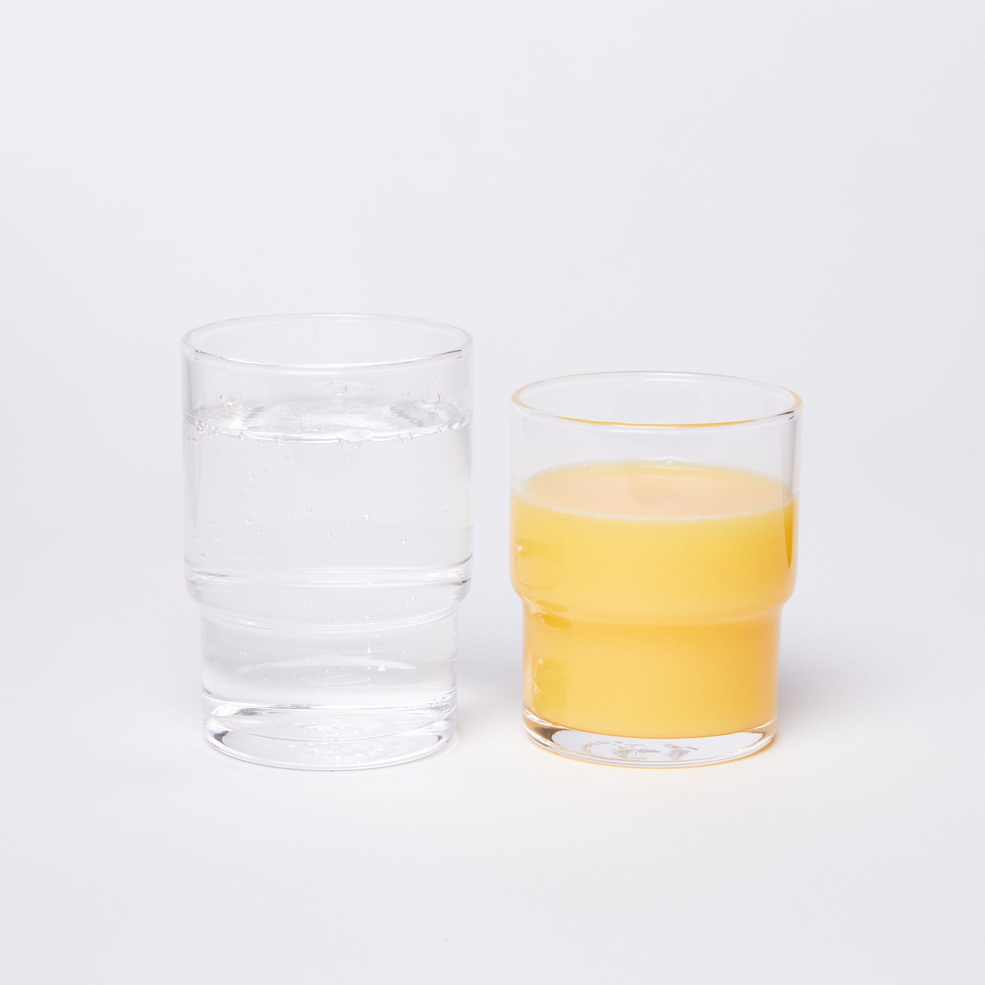 A taller glass full of water on the left next to a shorter glass full of orange juice on the right
