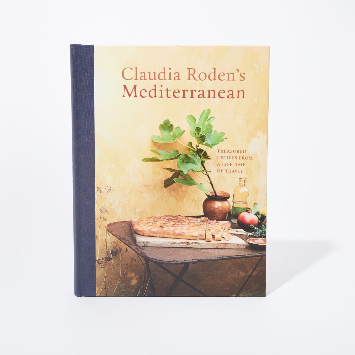 Cover of book with a photo of sliced focaccia on a cutting board next to a fig branch and pomegranate with the title above in a serif font, "Claudia Roden's Mediterranean"