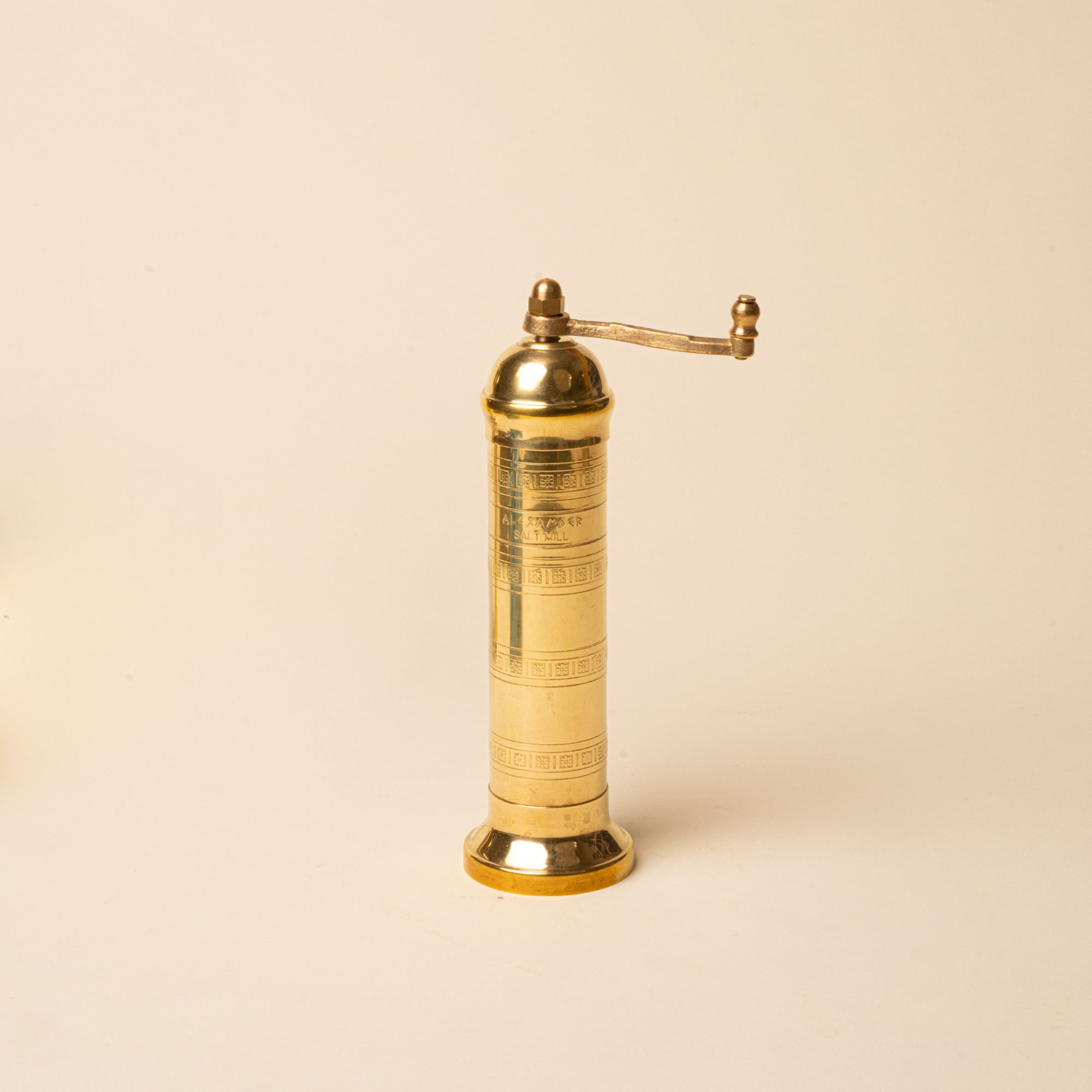Small brass salt mill with engraved details and a side handle on a neutral background.