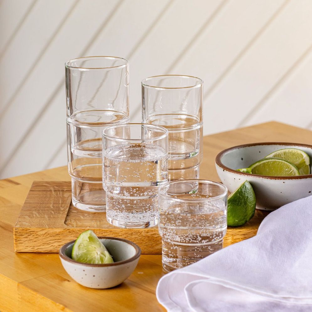 A tabletop filled with stacked small and large water glasses filled with seltzer, little bowls with lime slices, and a white linen napkin.