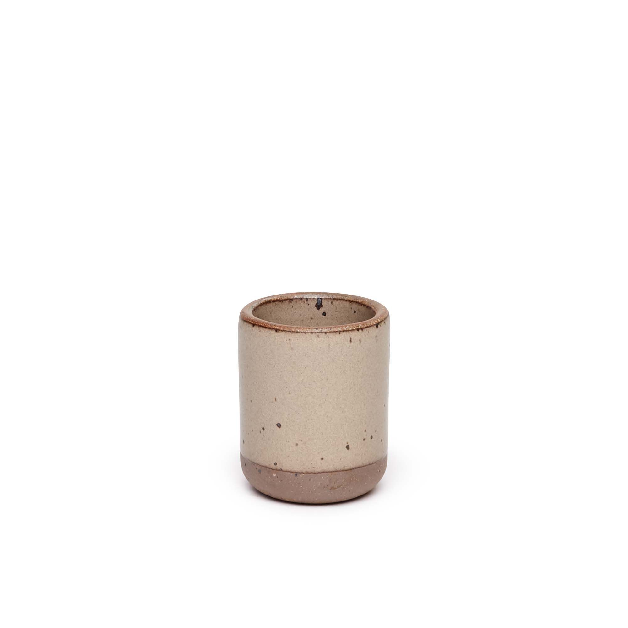 A small, short ceramic mug cup in a warm pale brown color featuring iron speckles and unglazed rim and bottom base.