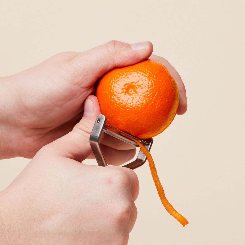 One hand grips a tangerine while the other hand peels a ribbon from tangerine.
