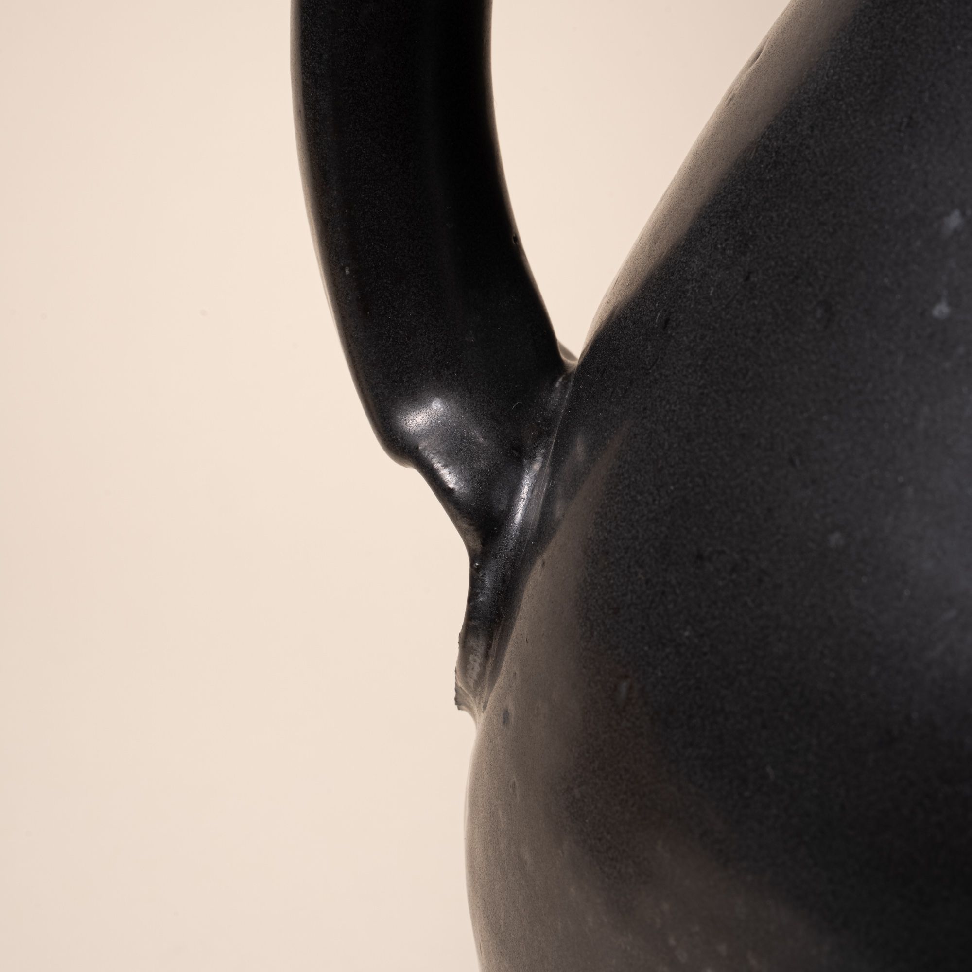 A closeup of the bottom of the handle connected to the body of a ceramic pitcher.