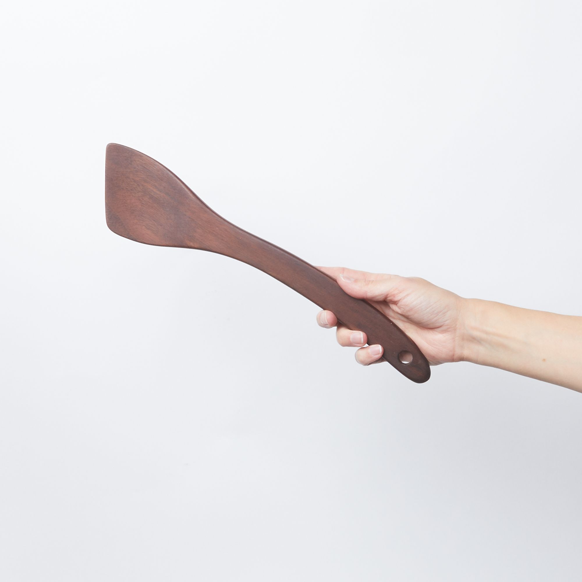 Hand holding a black walnut wood spatula with a slanted head and a hole at the bottom
