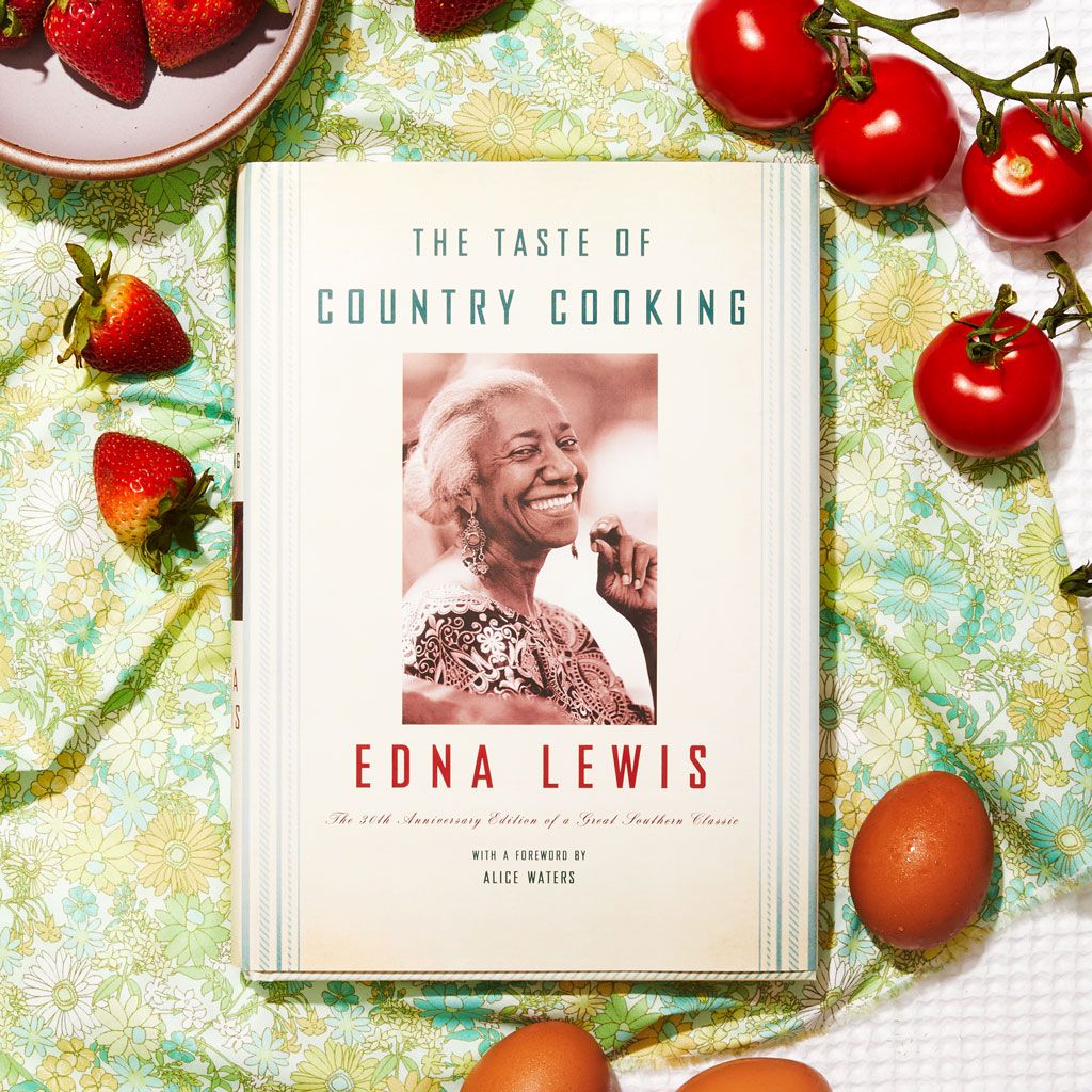 A copy of The Taste of Country Cooking with strawberries and tomatoes around it on a green and blue floral background