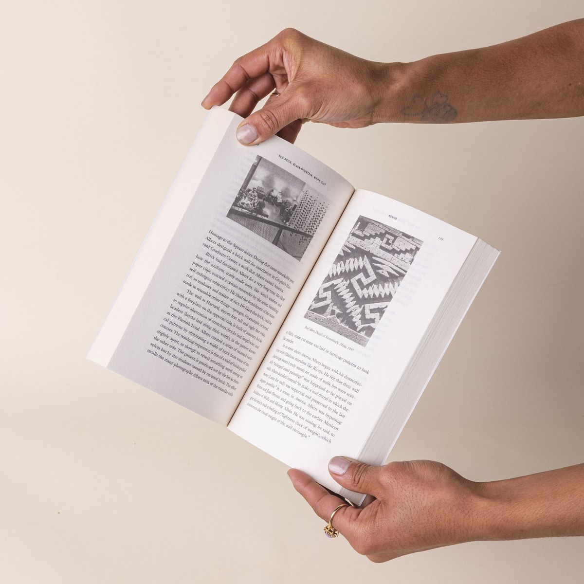 Hands open a paperback book with plain text and black and white photos