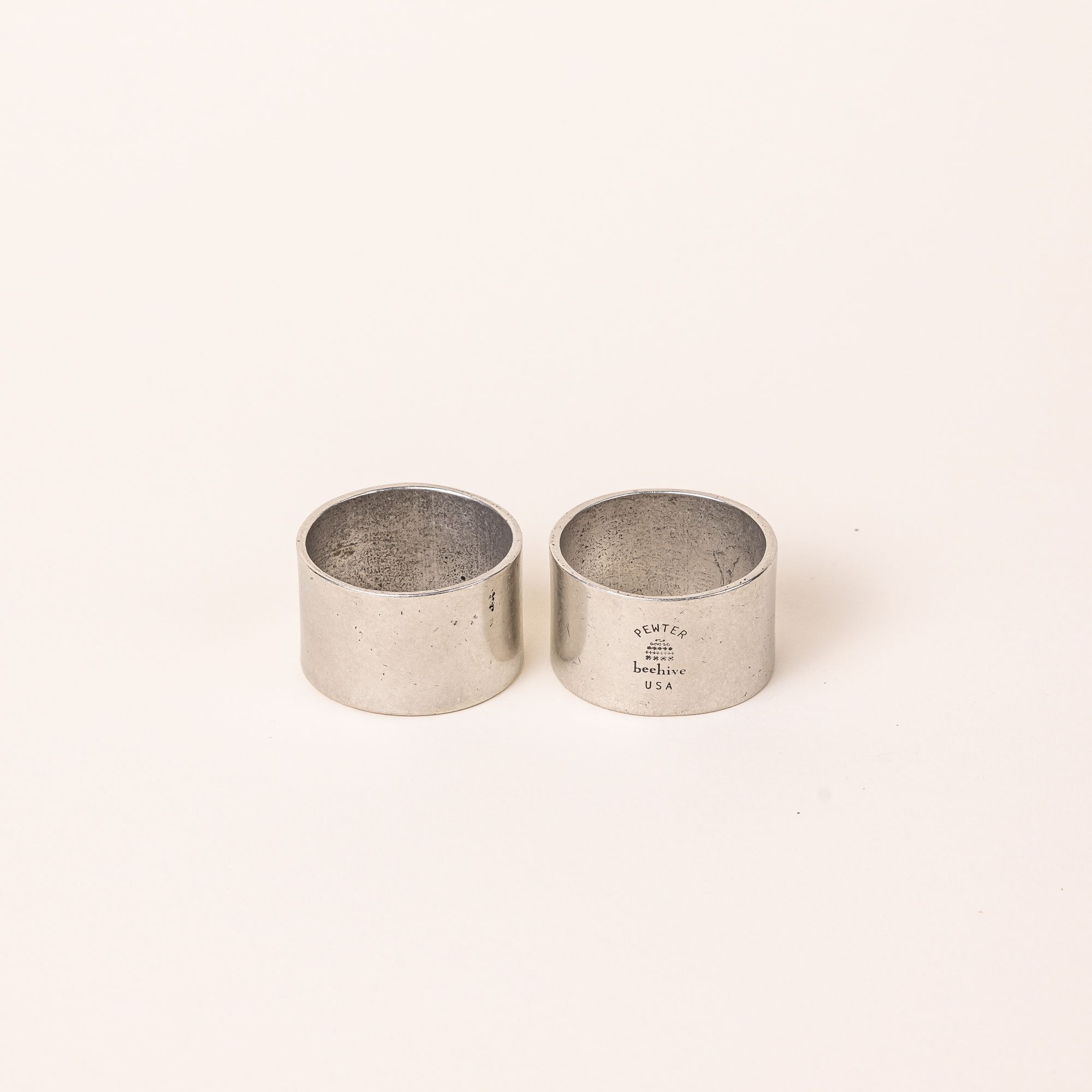 Two simple silver pewter napkin rings sitting together - the right has the maker's stamp.