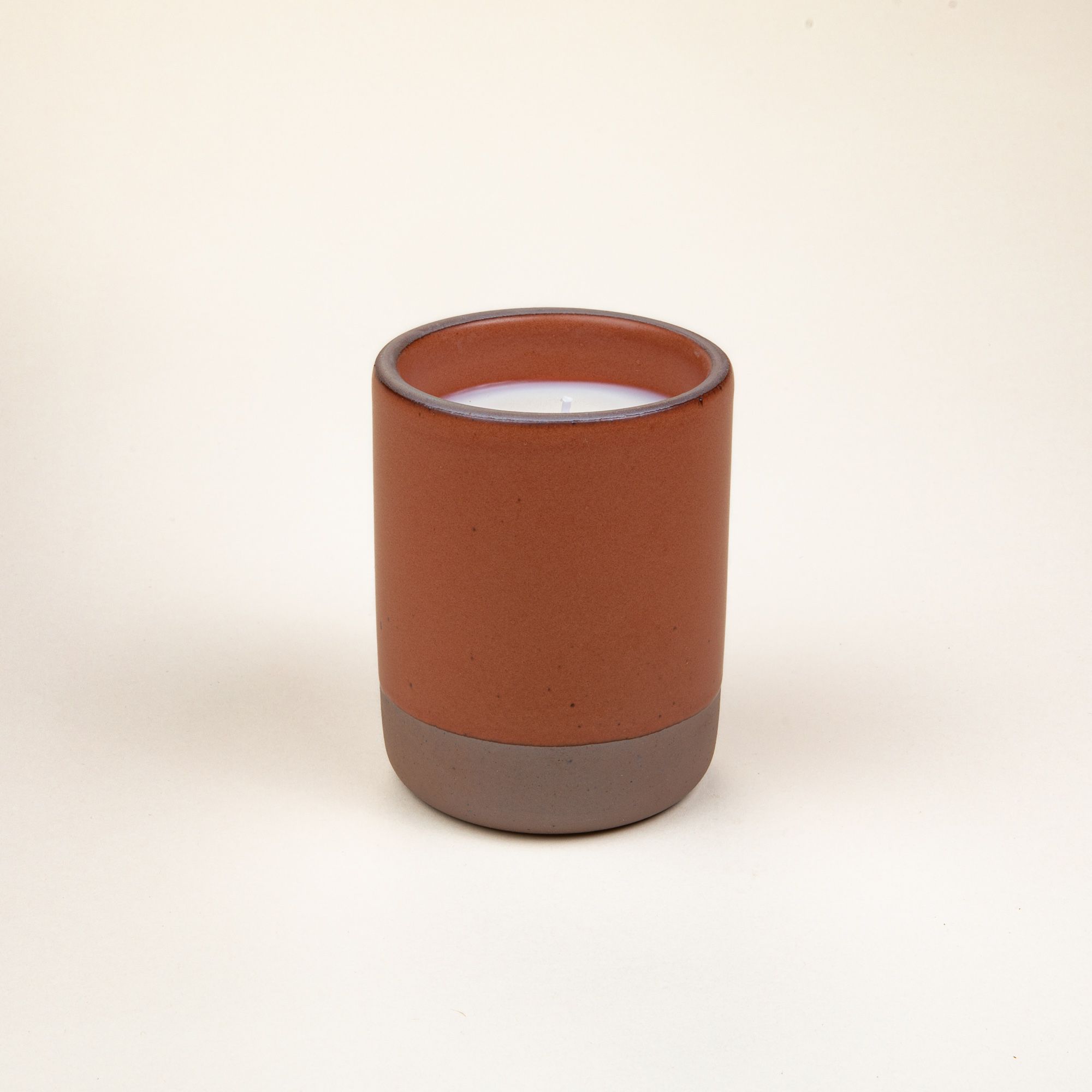 Large ceramic vessel in a cool terracotta color with candle inside.