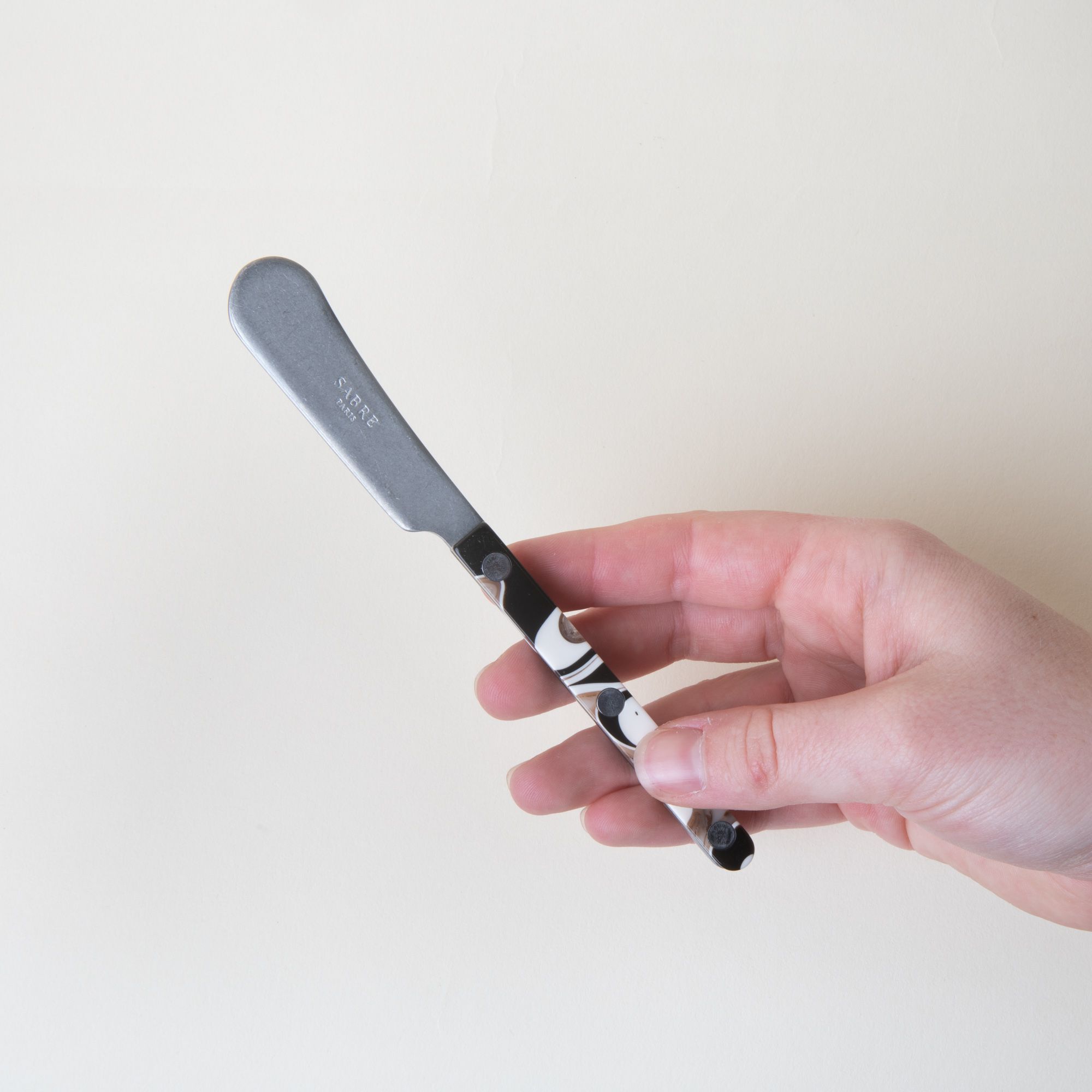 A hand holding a butter knife with a stainless steel blade and an acrylic black, white, and brown handle