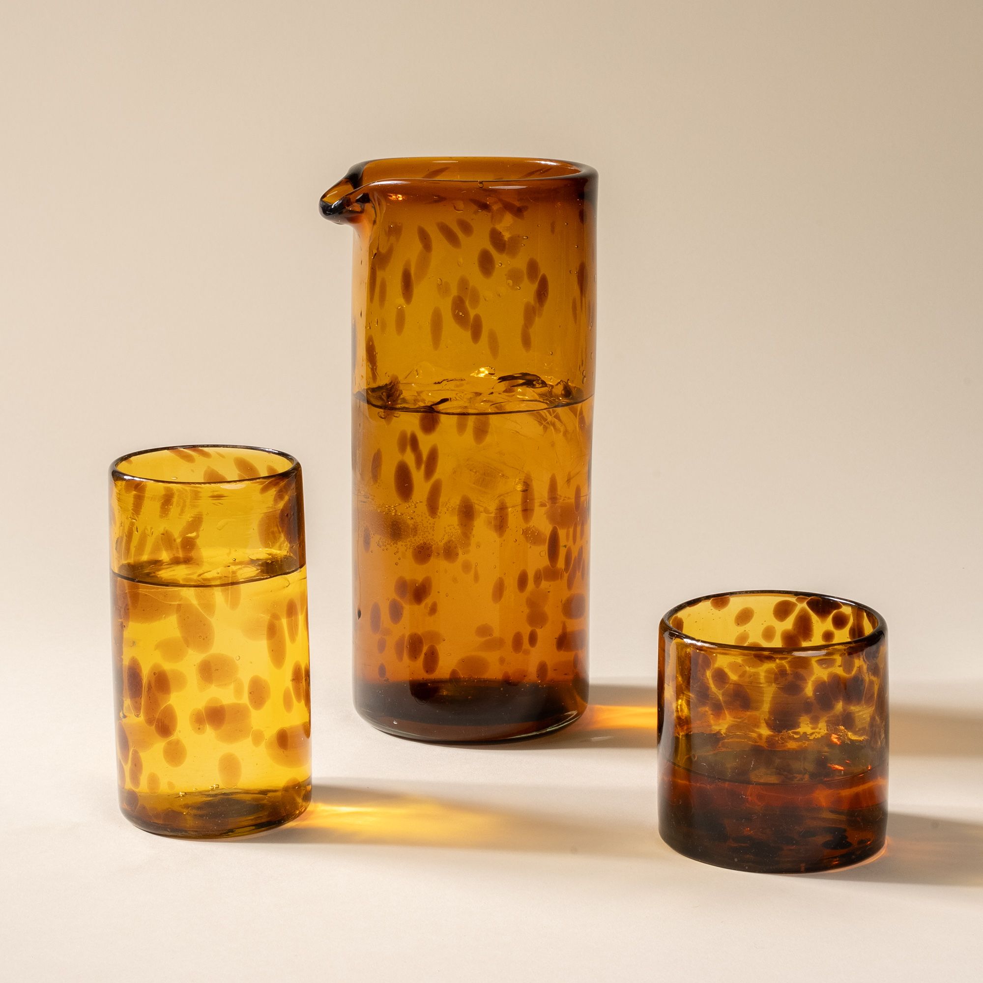 A tall tumbler, large pitcher, and short tumbler, of transparent glassware in a tortoiseshell pattern, all filled with drinks.
