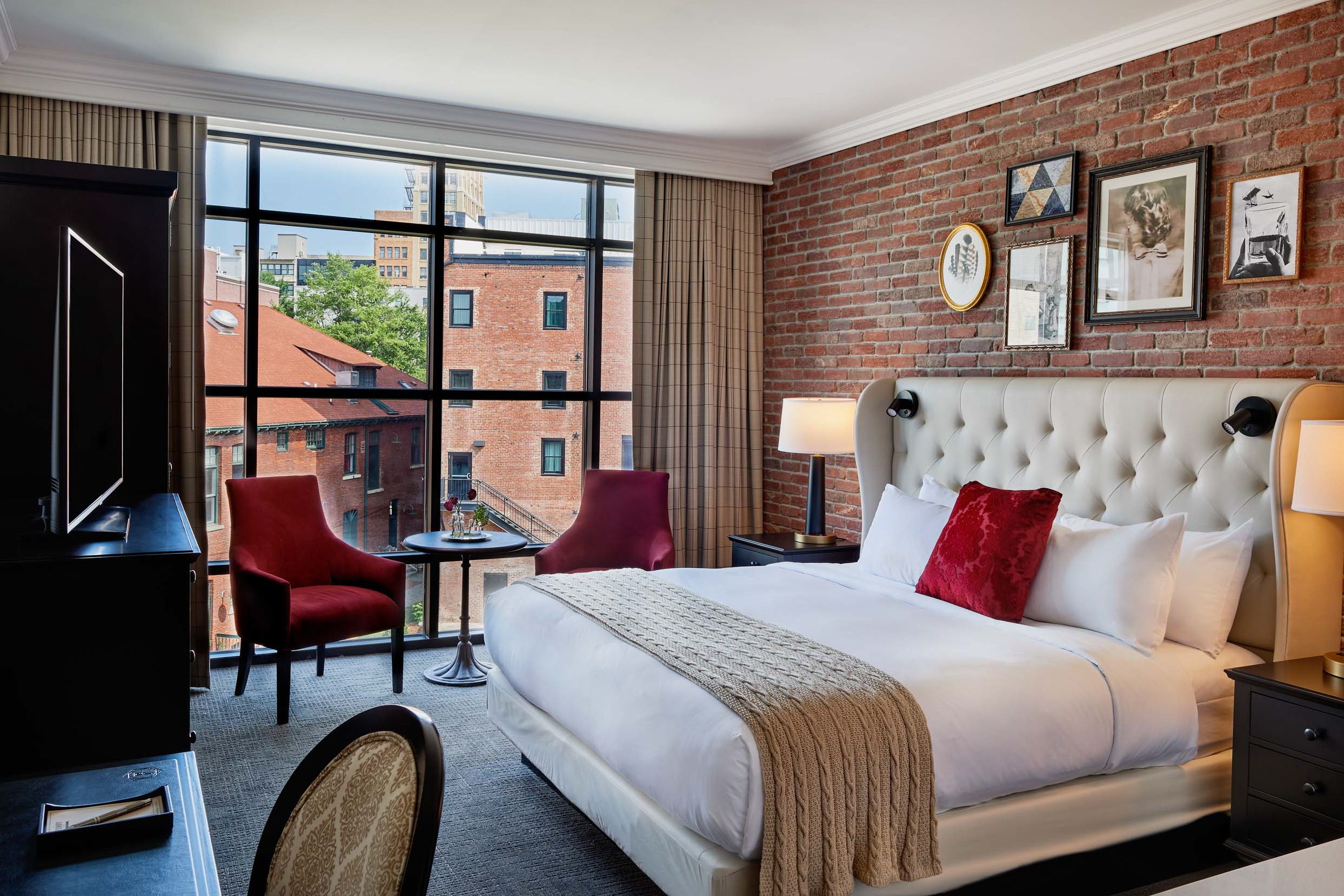 King Bedroom at Foundy Hotel in Asheville with large bed in the center of a brick wall and two velvet red chairs