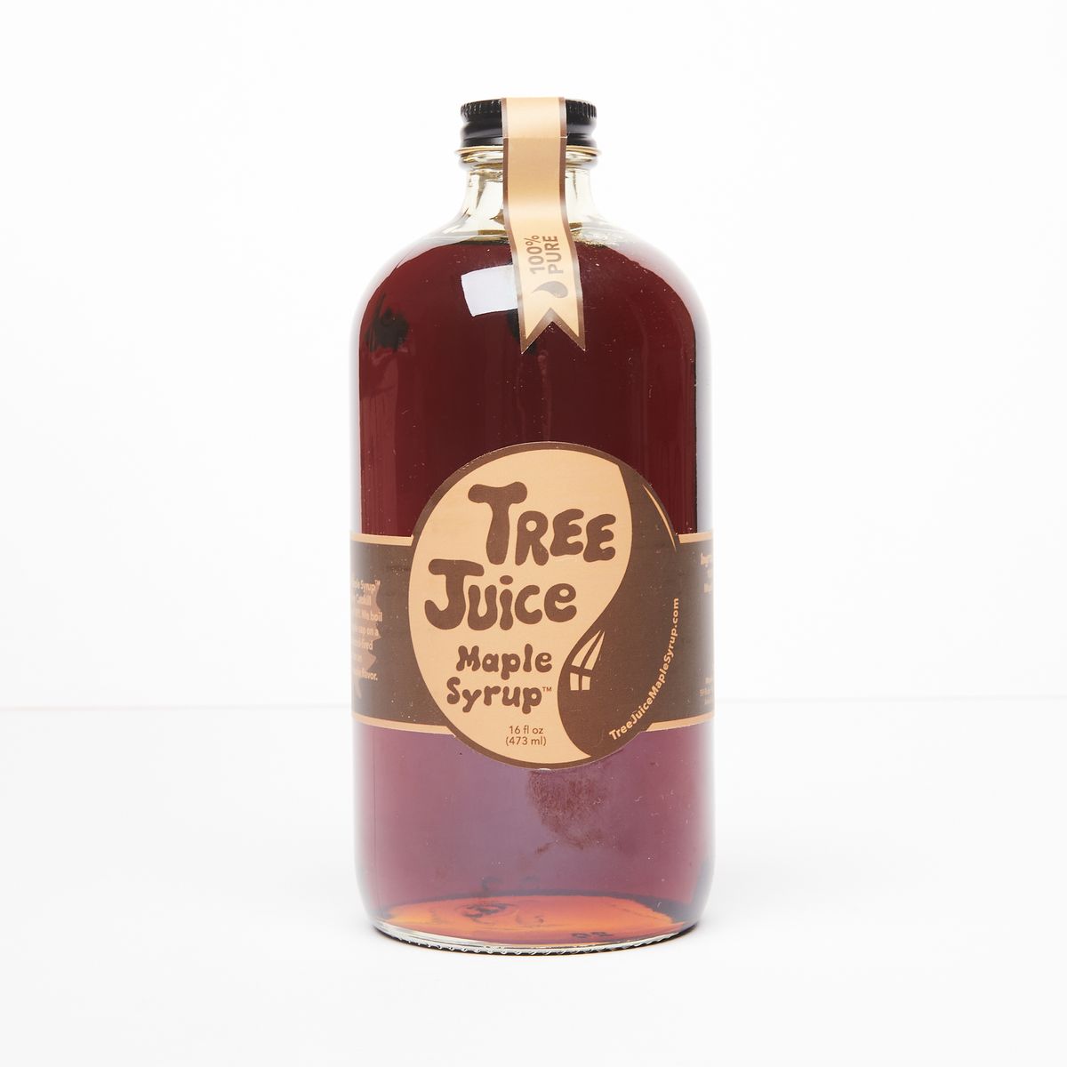 Glass bottle with black cap filled with brown syrup and a label that reads "Tree Juice Maple Syrup"