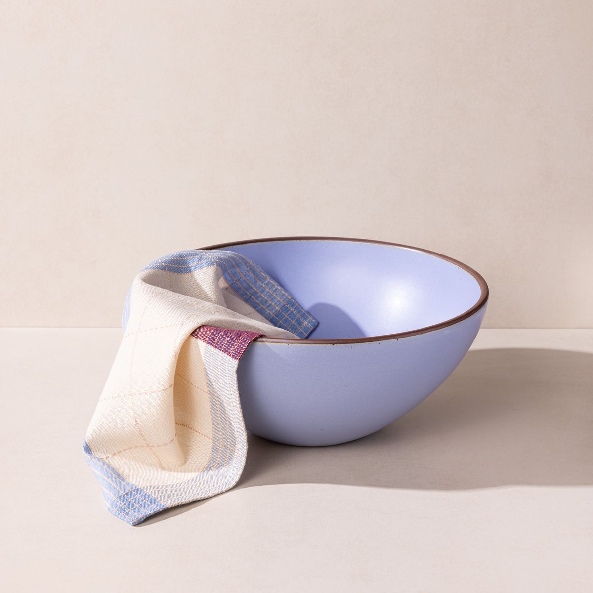 A dinner napkin hangs out of a large ceramic mixing bowl in a periwinkle color featuring iron speckles and an unglazed rim