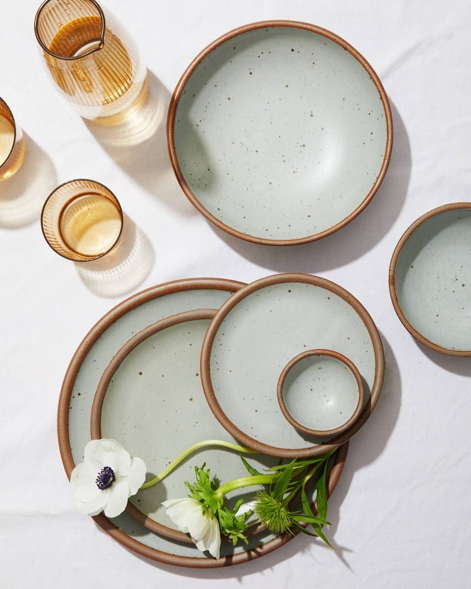 An artful arrangement of plates in various sizes in Soapstone, a light blue grey with some amber glasses and some anemones.