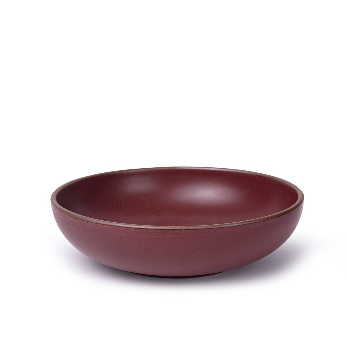 A large shallow serving ceramic bowl in a plum color featuring iron speckles and an unglazed rim.