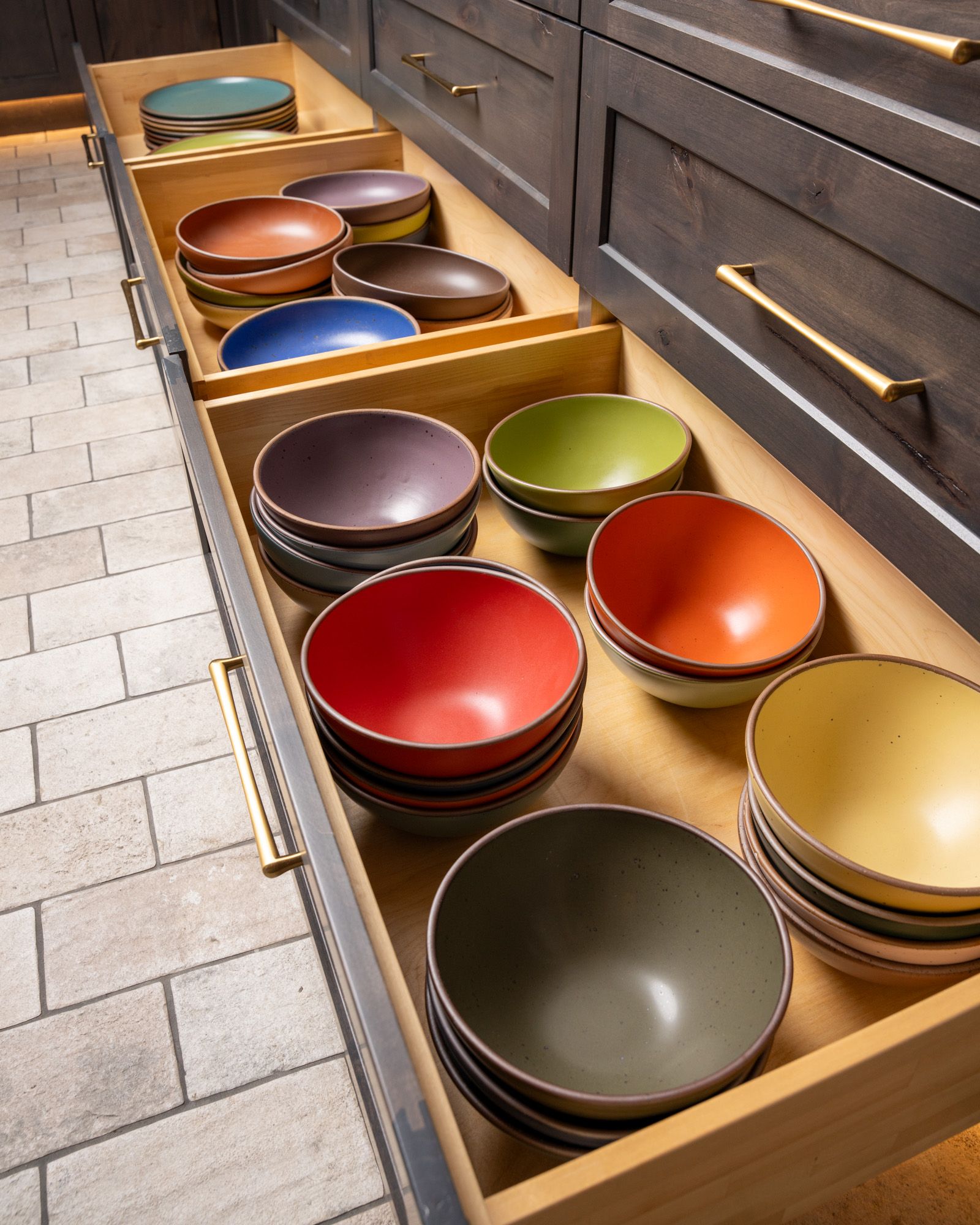 Open cabinet drawers are stacked with ceramic bowls in different colors of the rainbow.