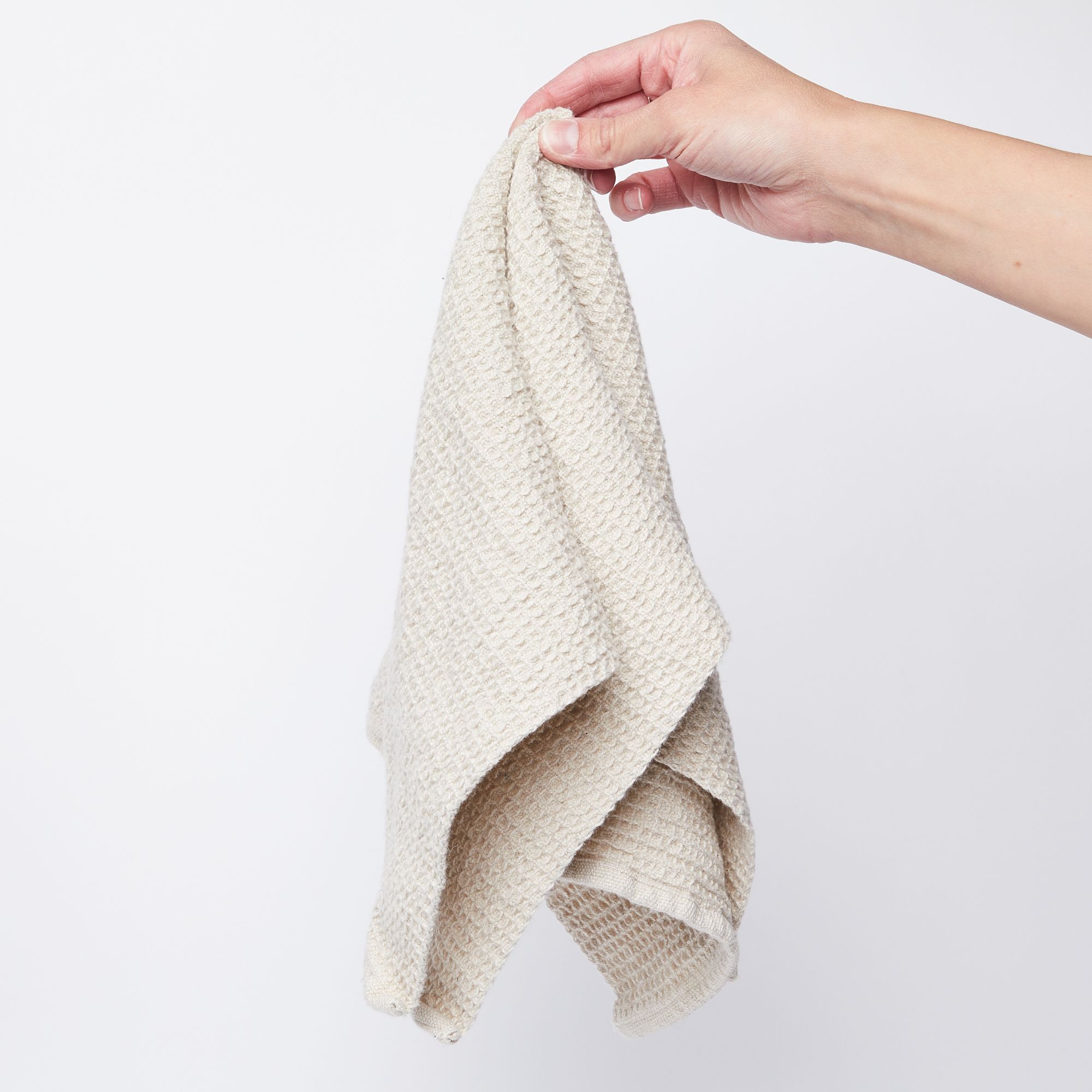 Hand holding a natural color waffle weave kitchen towel