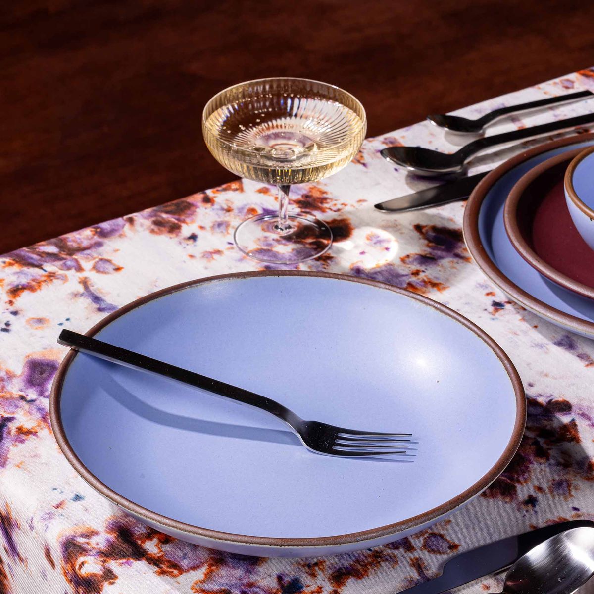 A large ceramic plate with a curved bowl edge in a periwinkle color on a table with a fork