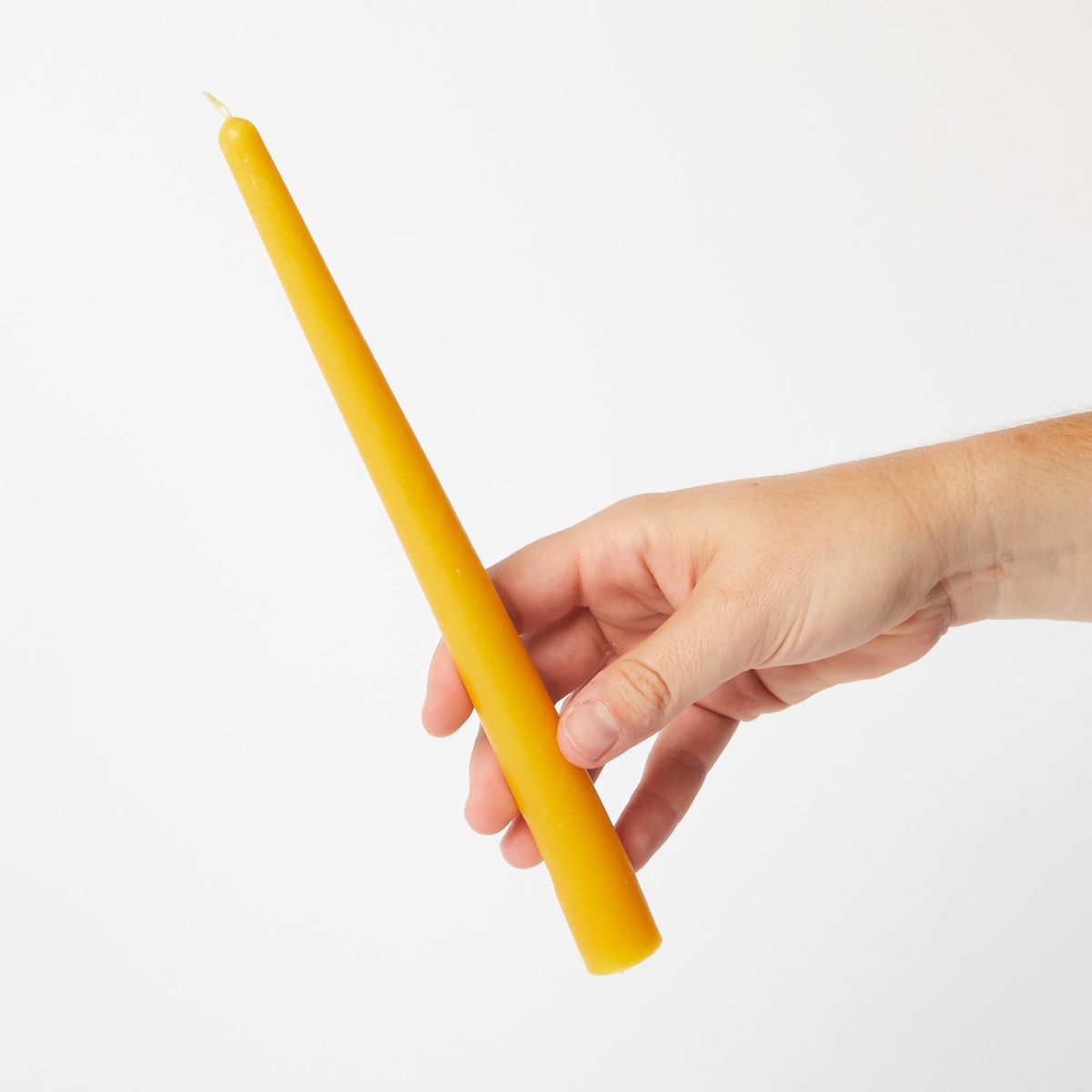 hand holding yellow beeswax taper candle