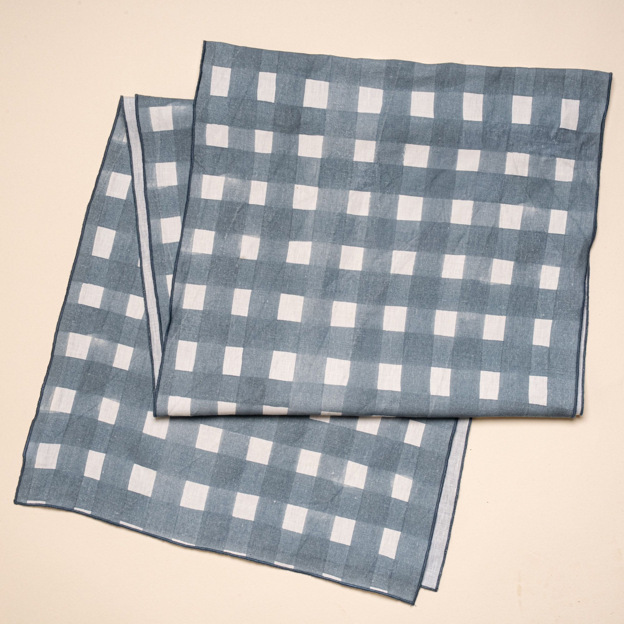 A table runner folded laying flat featuring a blue-grey crosshatch pattern with navy edges.