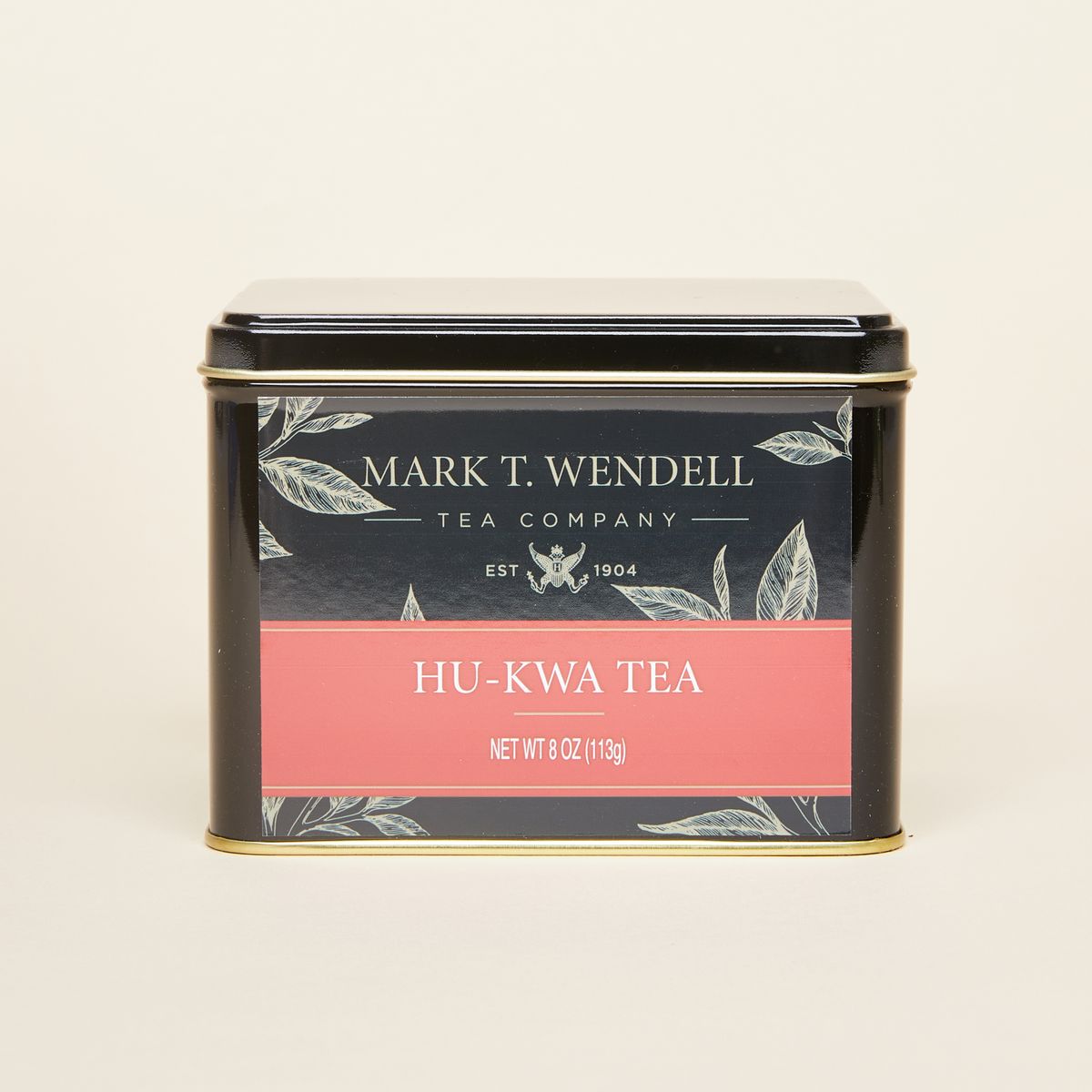 A small pile of black tea sits beside a tin box in black with gold and red details. Words read "Mark T. Wendell Tea Company" and "Hu-Kwa Tea"