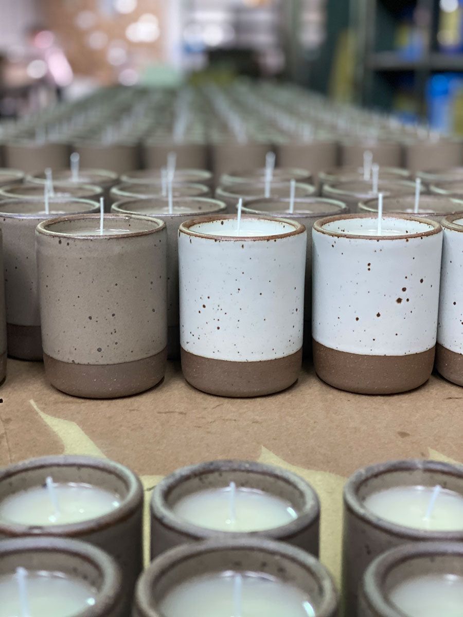East Fork ceramic vessels with unglazed rims and bottoms and featuring iron speckles are lined up for candle production with wicks sticking out of each vessel