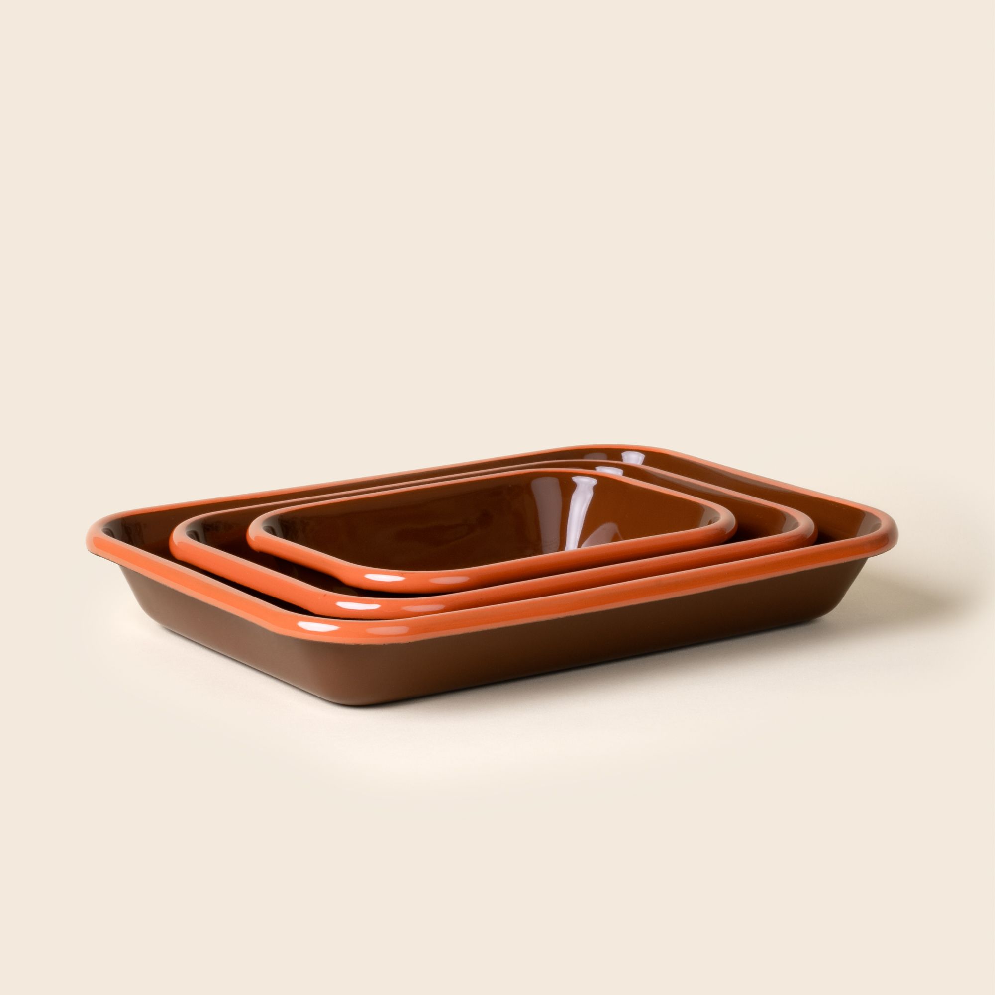 A nesting trio of small, medium, and large rectangular baking dishes in a dark red-brown color with an orange rim.