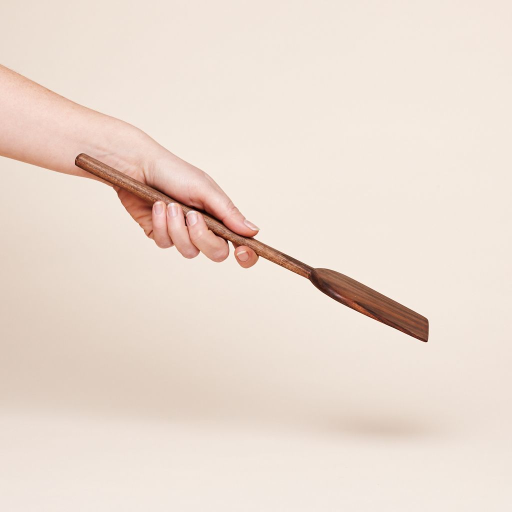 Held by a hand at a downward angle is a walnut wood handle that ends in a rectangle that is rounded at one end