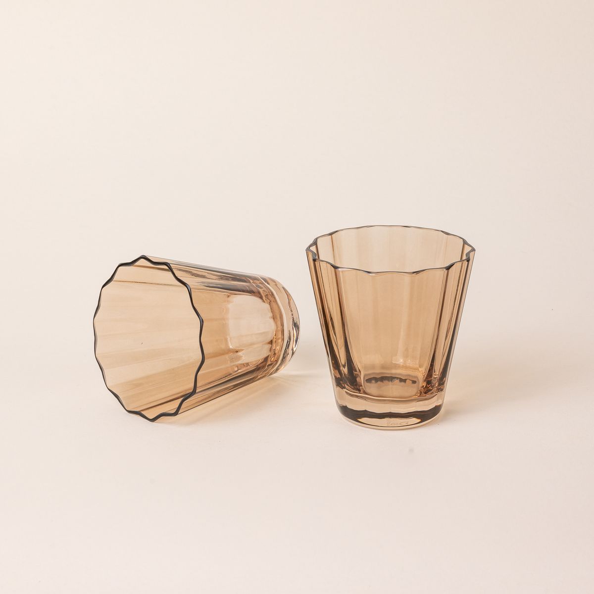 Two transparent light amber glasses with wide grooves on the site. One sits up right, and one is on its side.