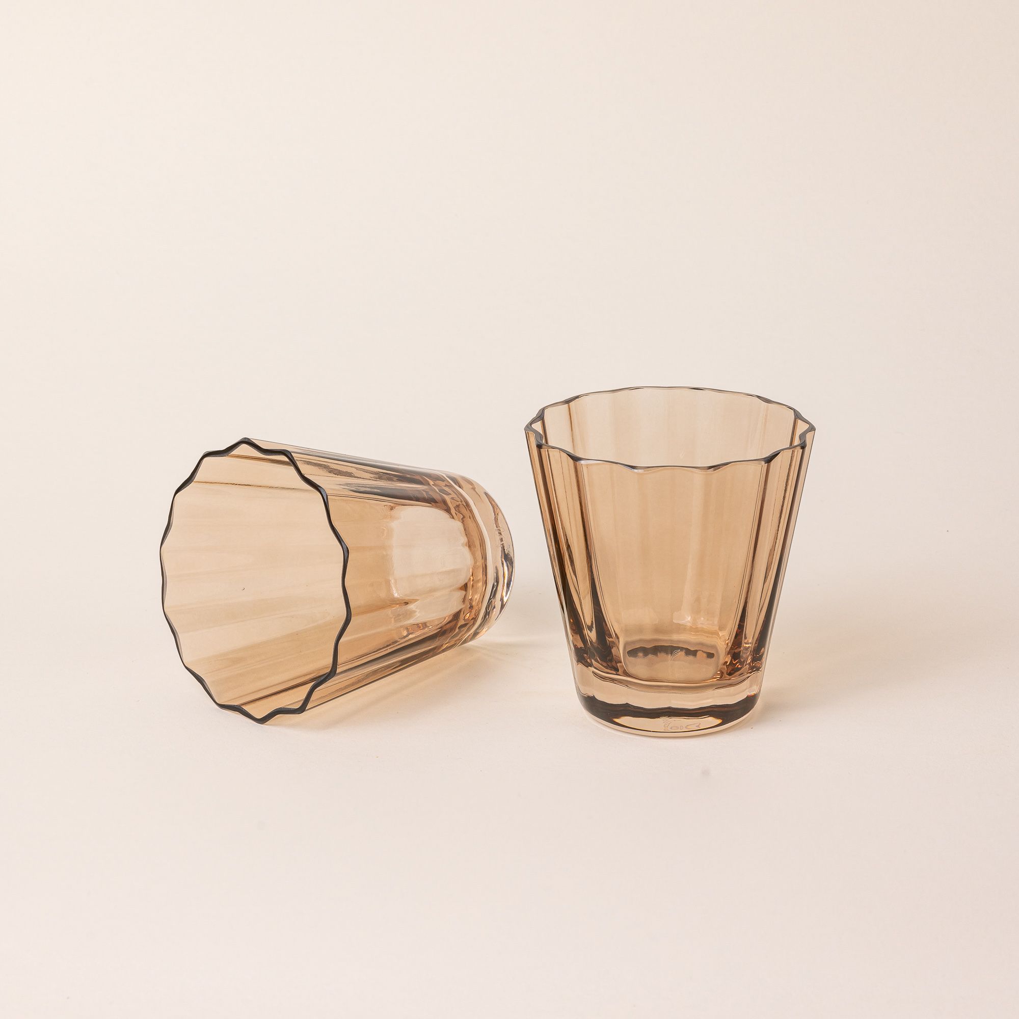 Two transparent light amber glasses with wide grooves on the side. One sits up right, and one is on its side.