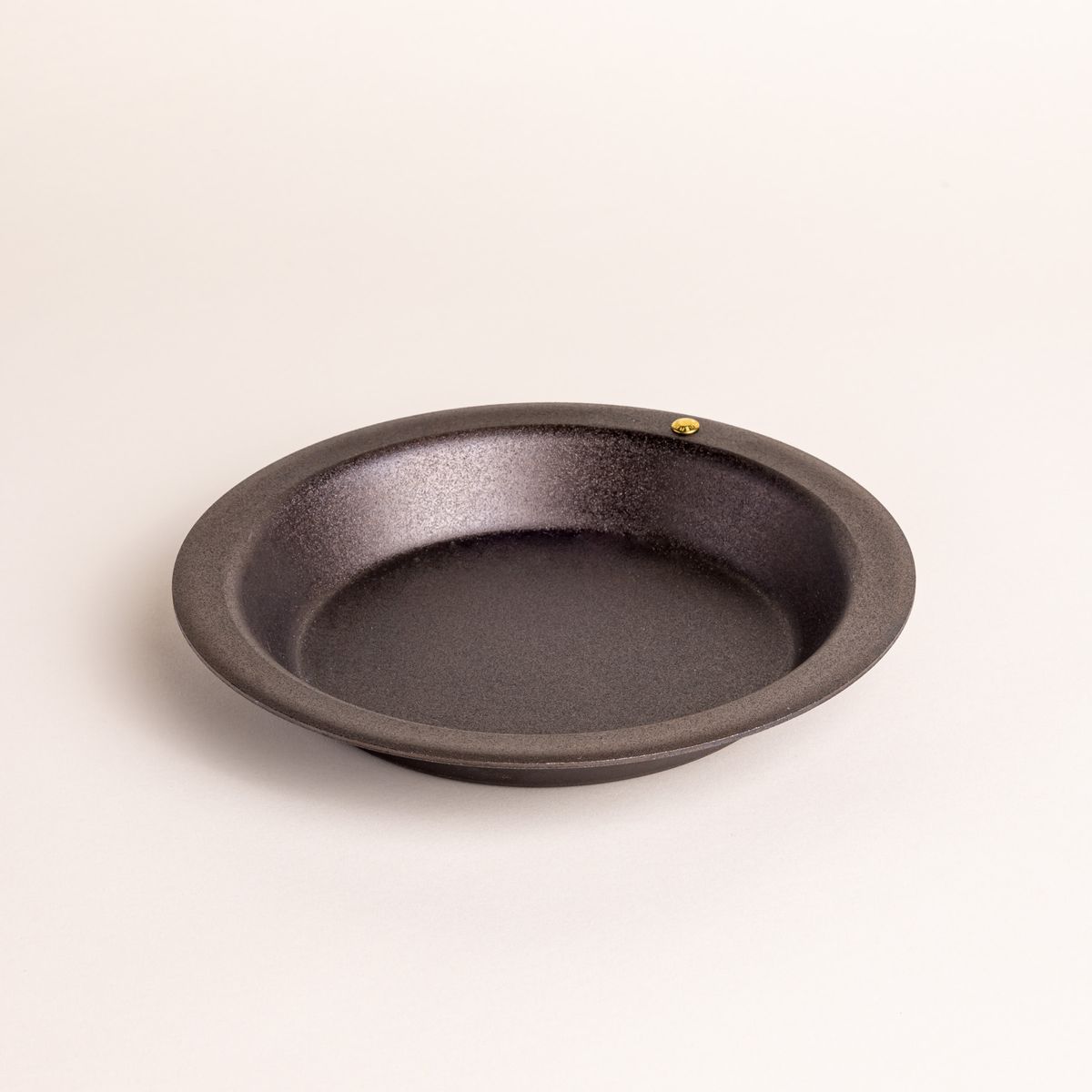 A small simple iron pie dish with a wide rim and shallow body