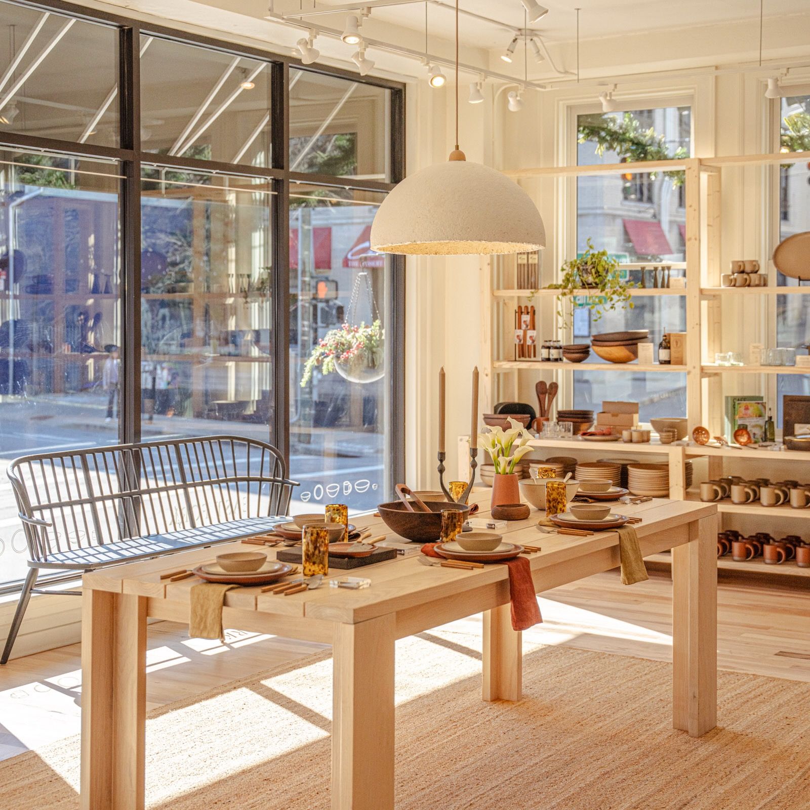 Inside of East Fork Asheville with large windows, shelves of pottery, and a wood table filled with place settings.