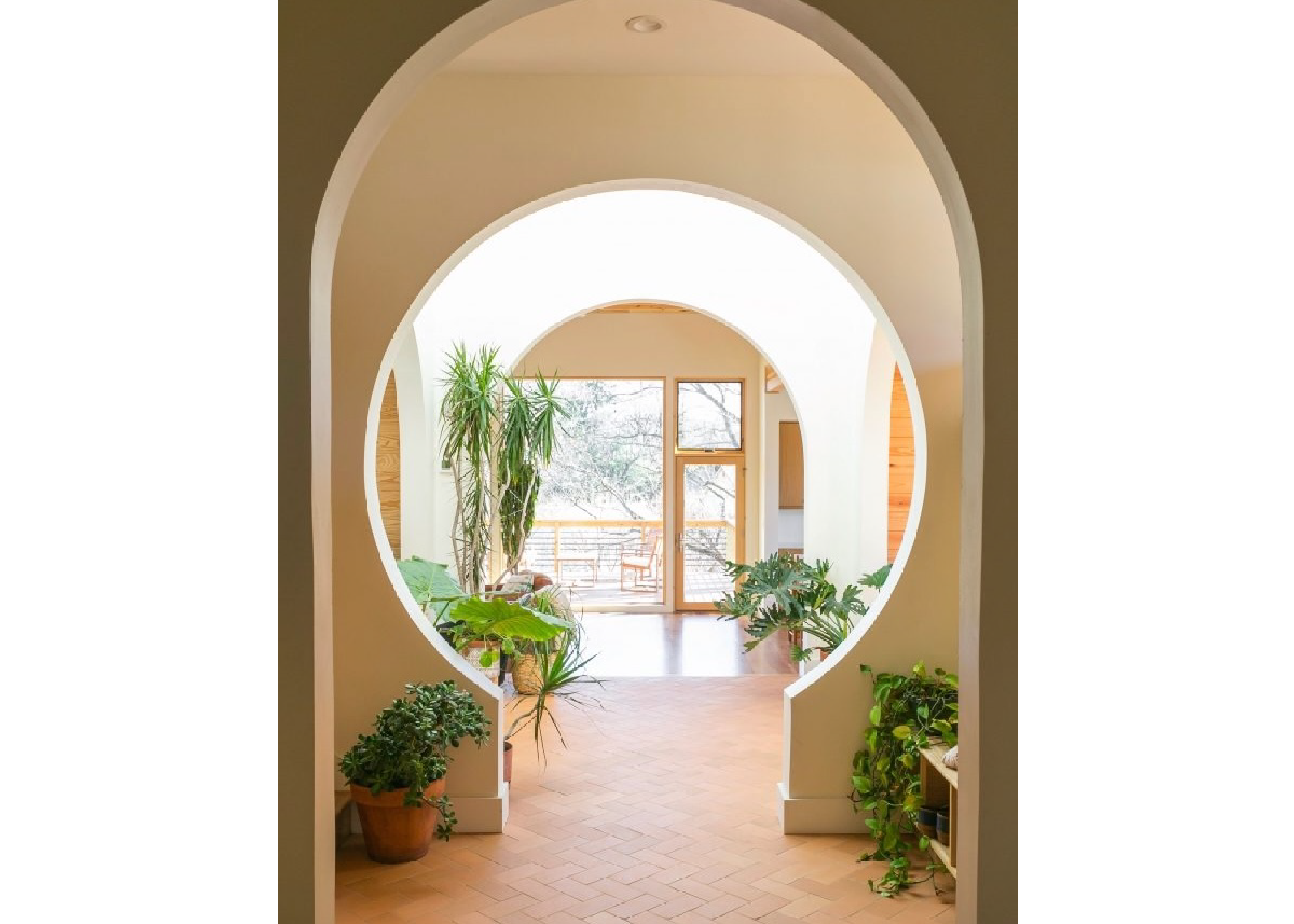 A home's atrium featuring several arches, potted plants, with tiled floors and large windows.