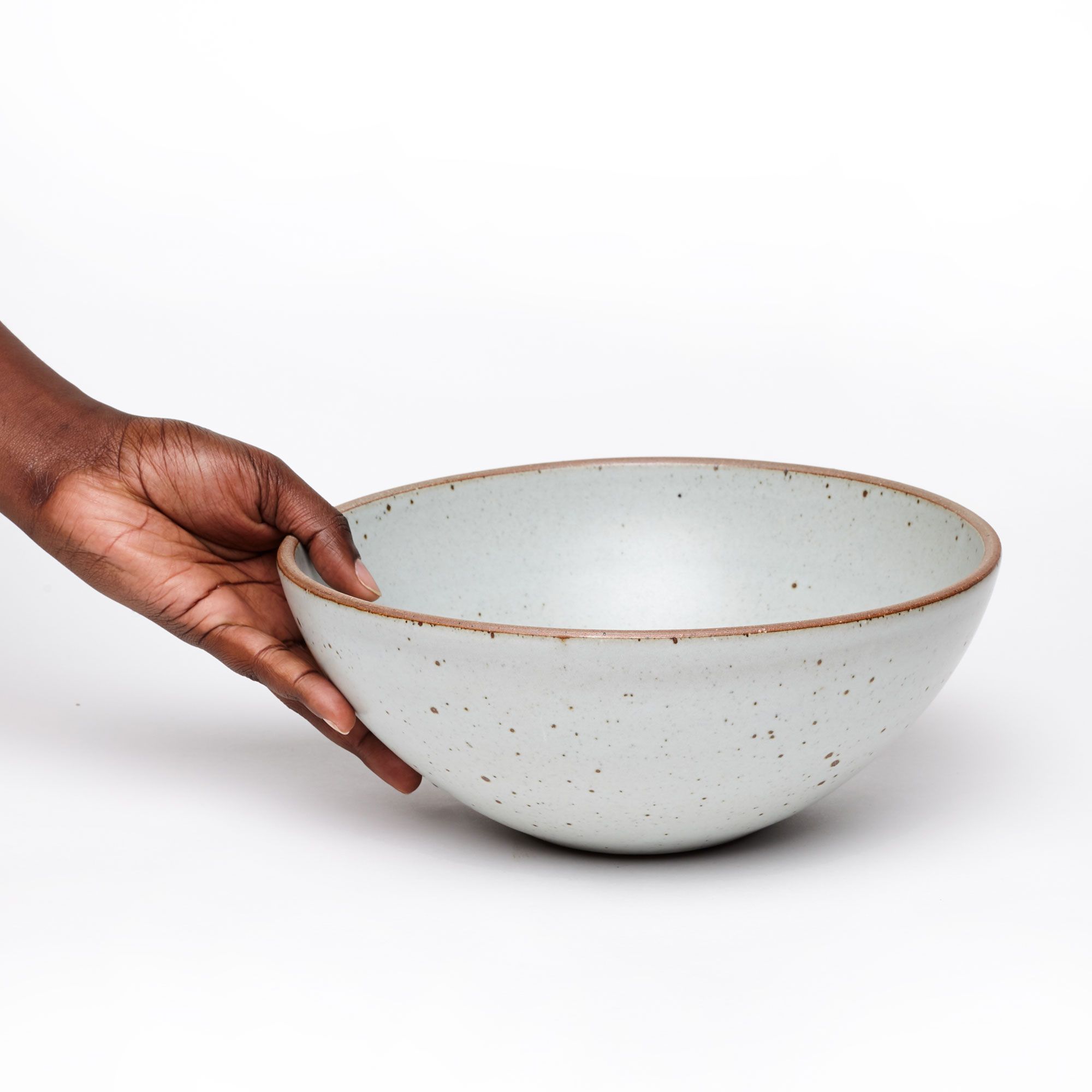 A hand holds a large ceramic bowl with an unglazed rim in a light gray color