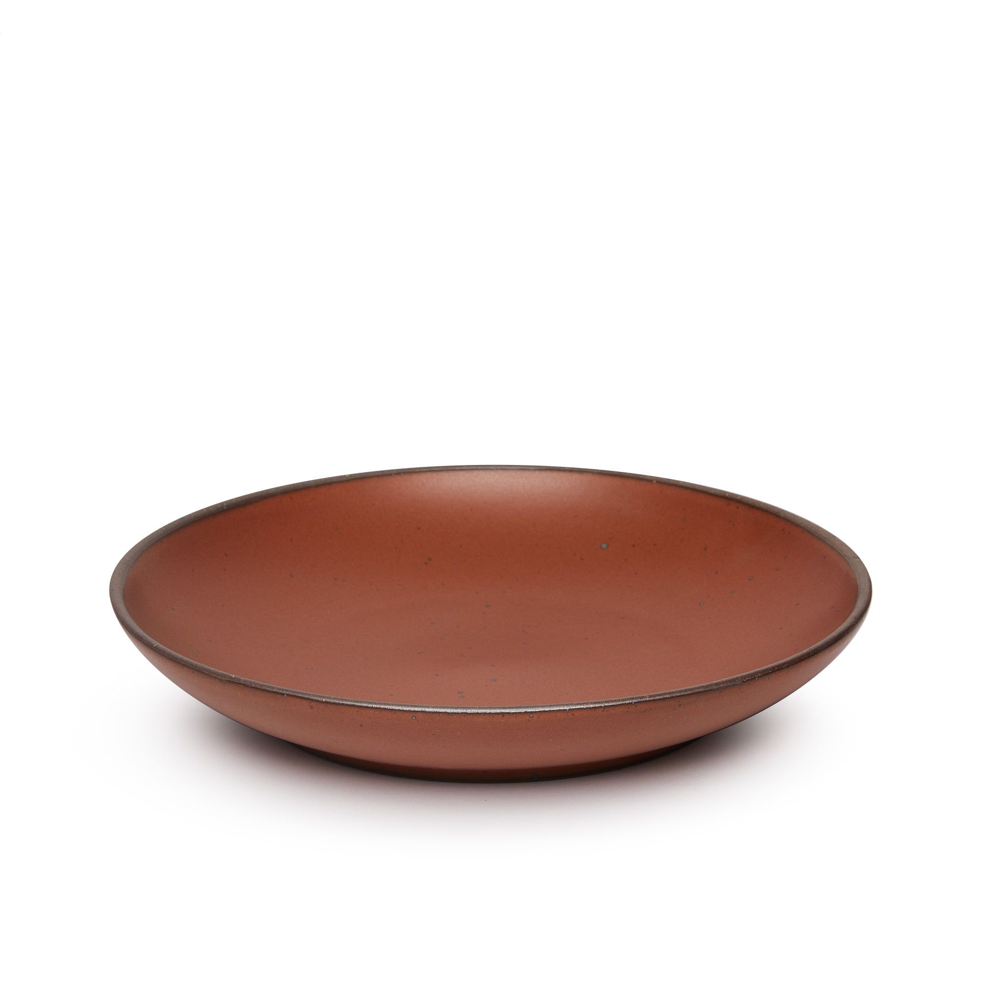 A large ceramic plate with a curved bowl edge in a cool burnt terracotta color featuring iron speckles and an unglazed rim.