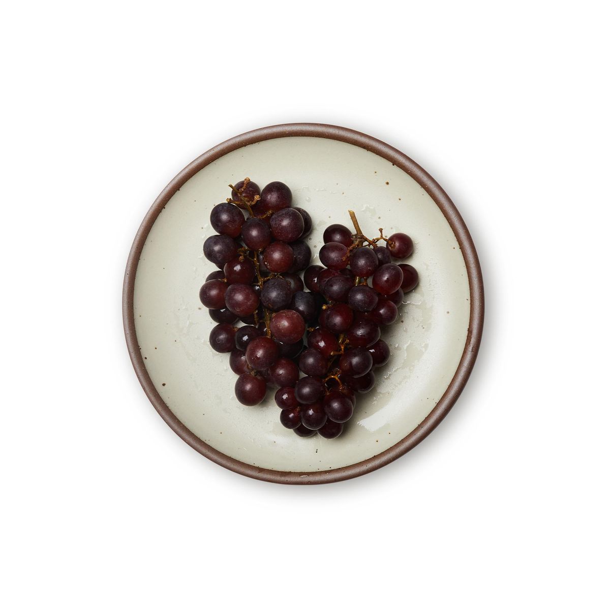 Grapes on a dinner sized ceramic plate in a warm, tan-toned, off-white color featuring iron speckles and an unglazed rim.